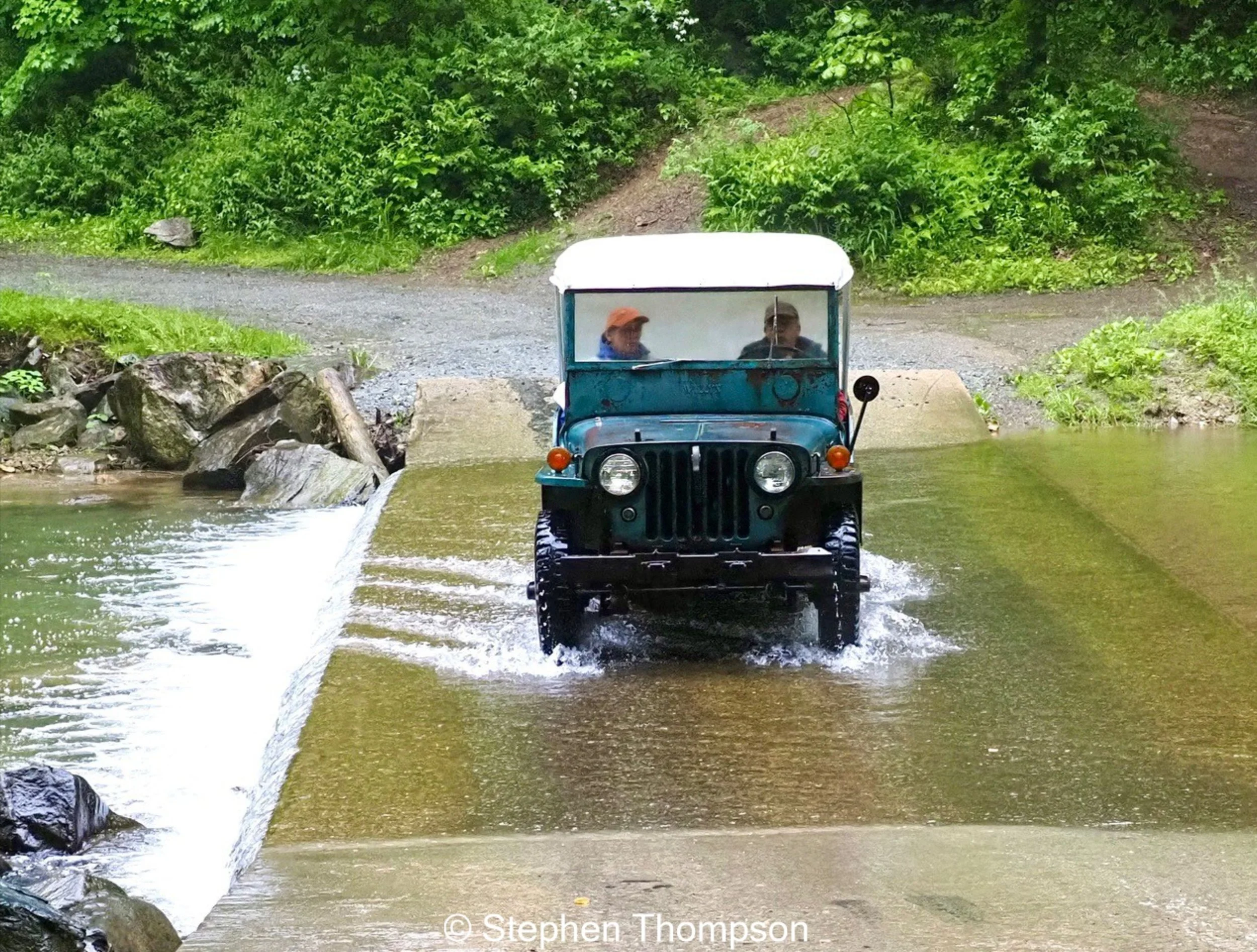 Old blue Jeep driving over bride with water running across bridge