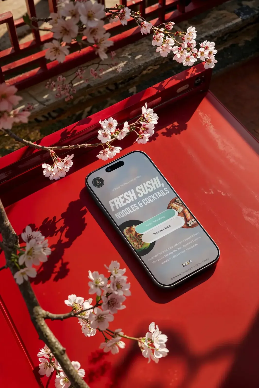A smartphone on a red table displays a restaurant app for ordering food, with cherry blossoms and a sunlight shadow surrounding it.