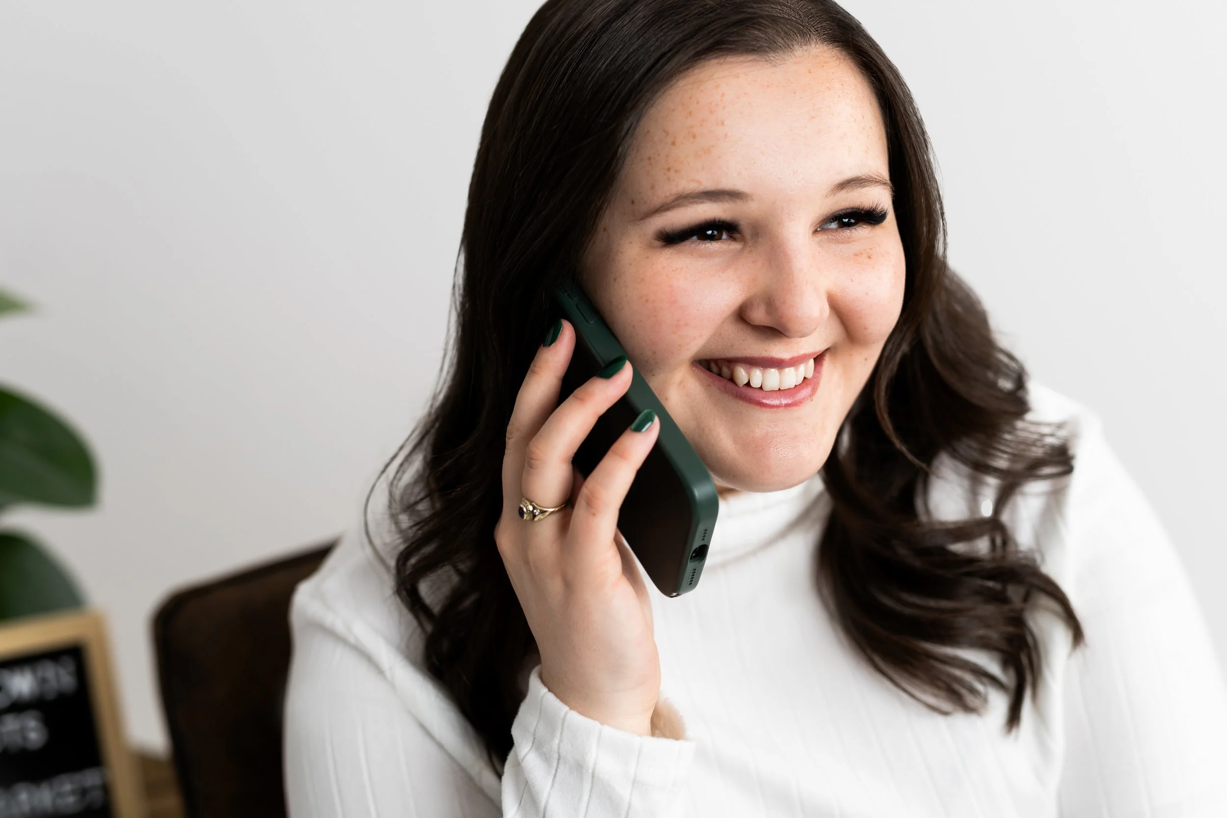 A smiling woman with dark brown hair talking on a green landline phone.
