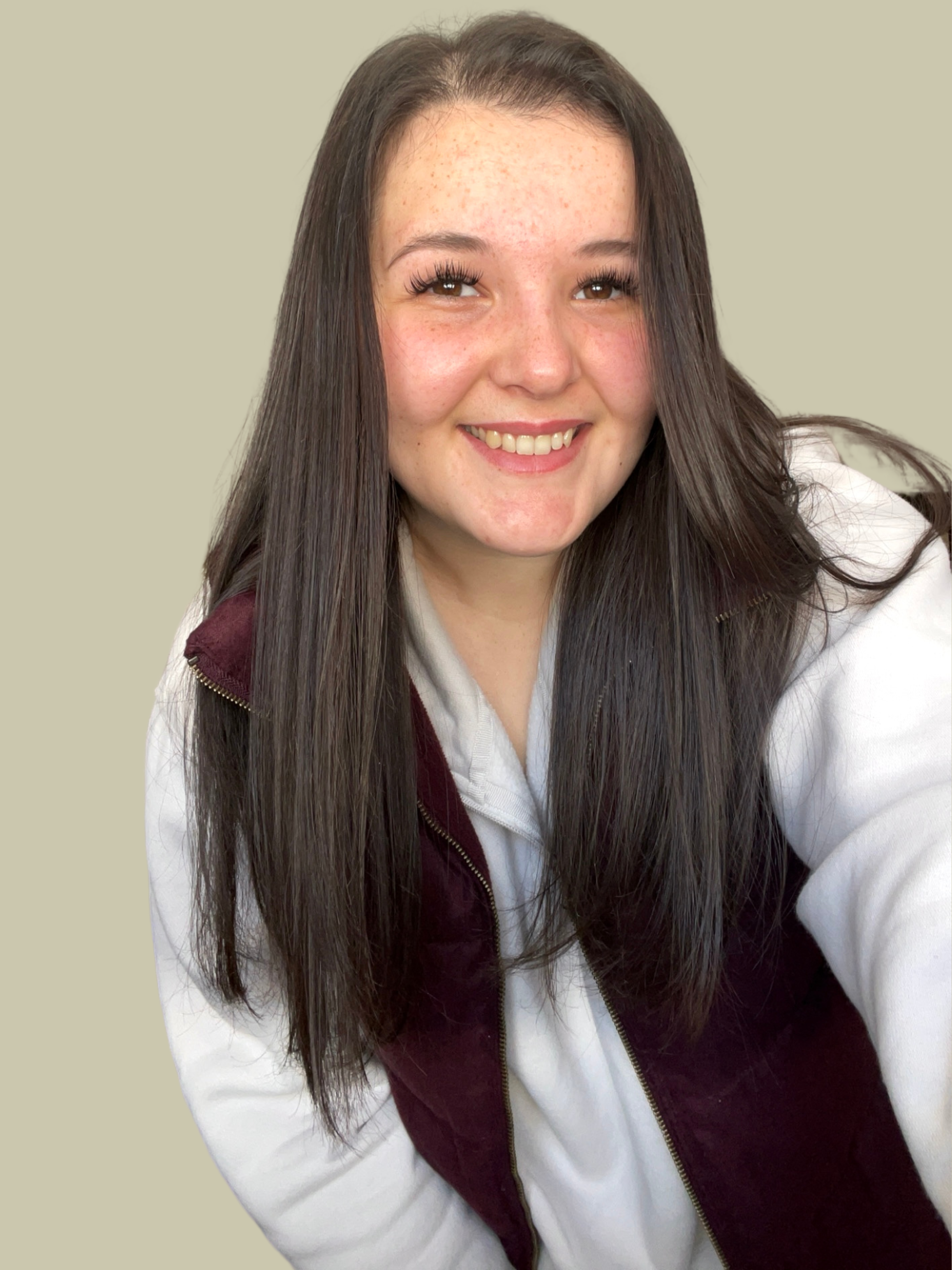 Young woman smiling, with long dark hair, wearing a white jacket and a maroon vest, against a plain beige background.