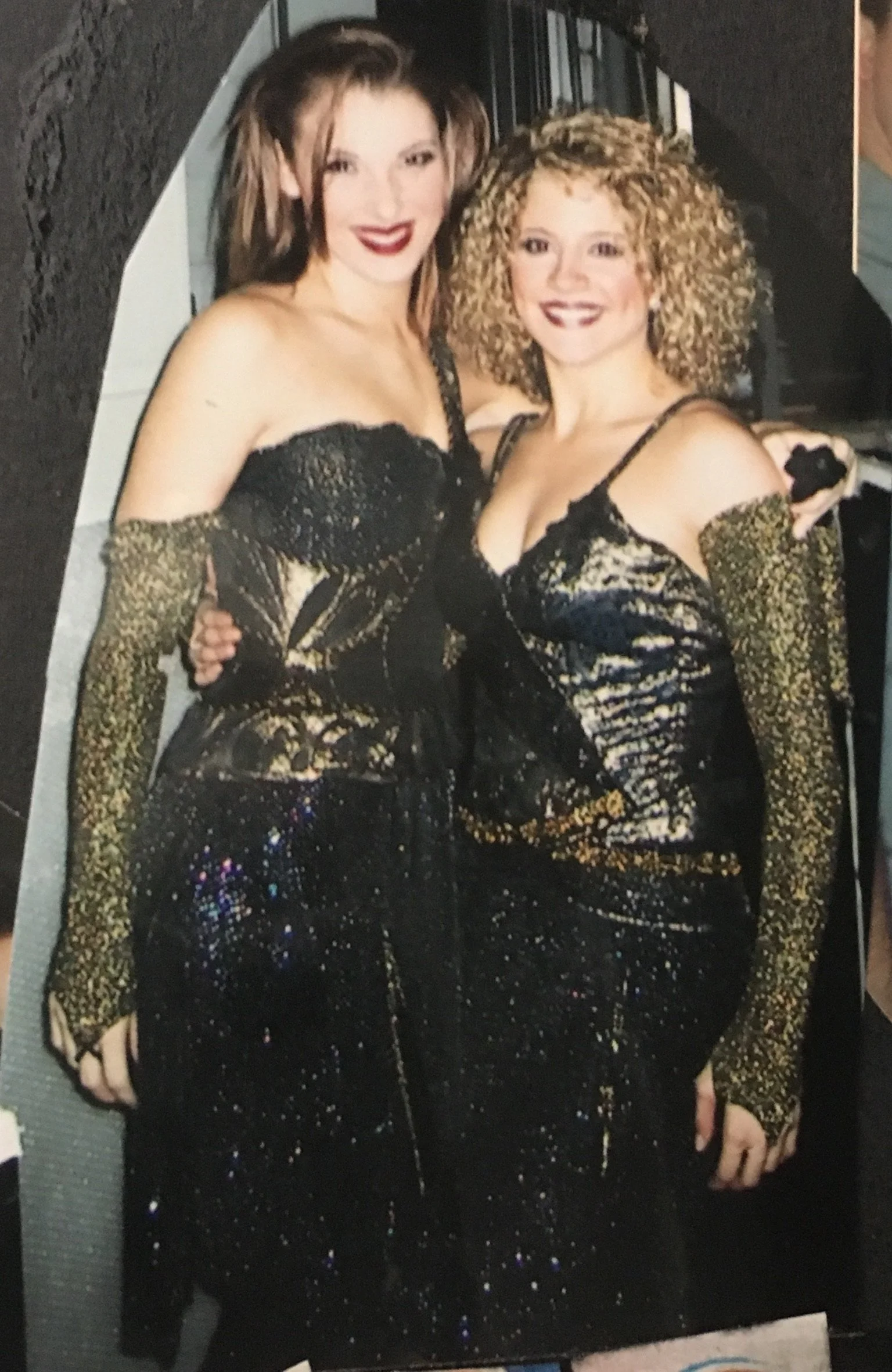 Two women in black and gold sequined dresses and matching gloves posing together at a formal event.