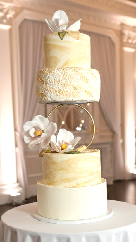 Bespoke golden, elegant four-tiered wedding cake for 100 guests. Features wafer paper, handcrafted Magnolia flowers, and three custom flavours, including a Gluten-Free Almond Spice top tier—luxury wedding cakes in Calgary by Magnolia Couture Cakery.