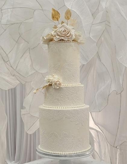Elegant double-tiered white wedding cake with floral decorating set to the bridal dress lace and a unique gold ring support on a cake stand. Bespoke luxury wedding cakes in Calgary by Magnolia Couture Cakery.