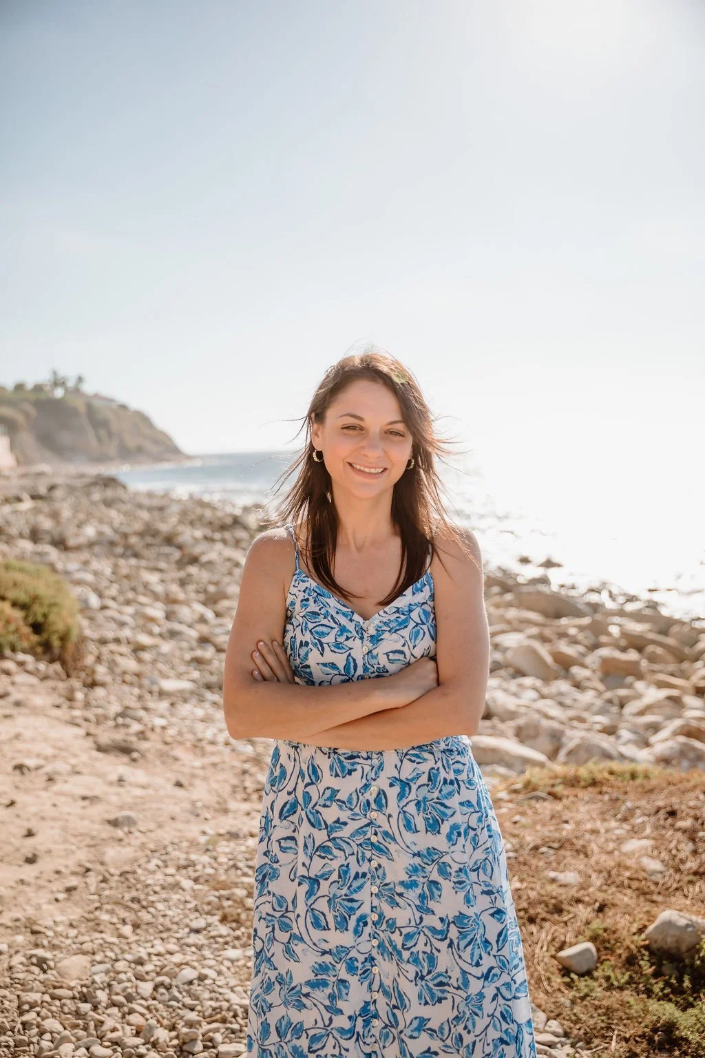 Morgan Abraham, LCSW, standing on a rocky beach with arms crossed and the ocean behind her