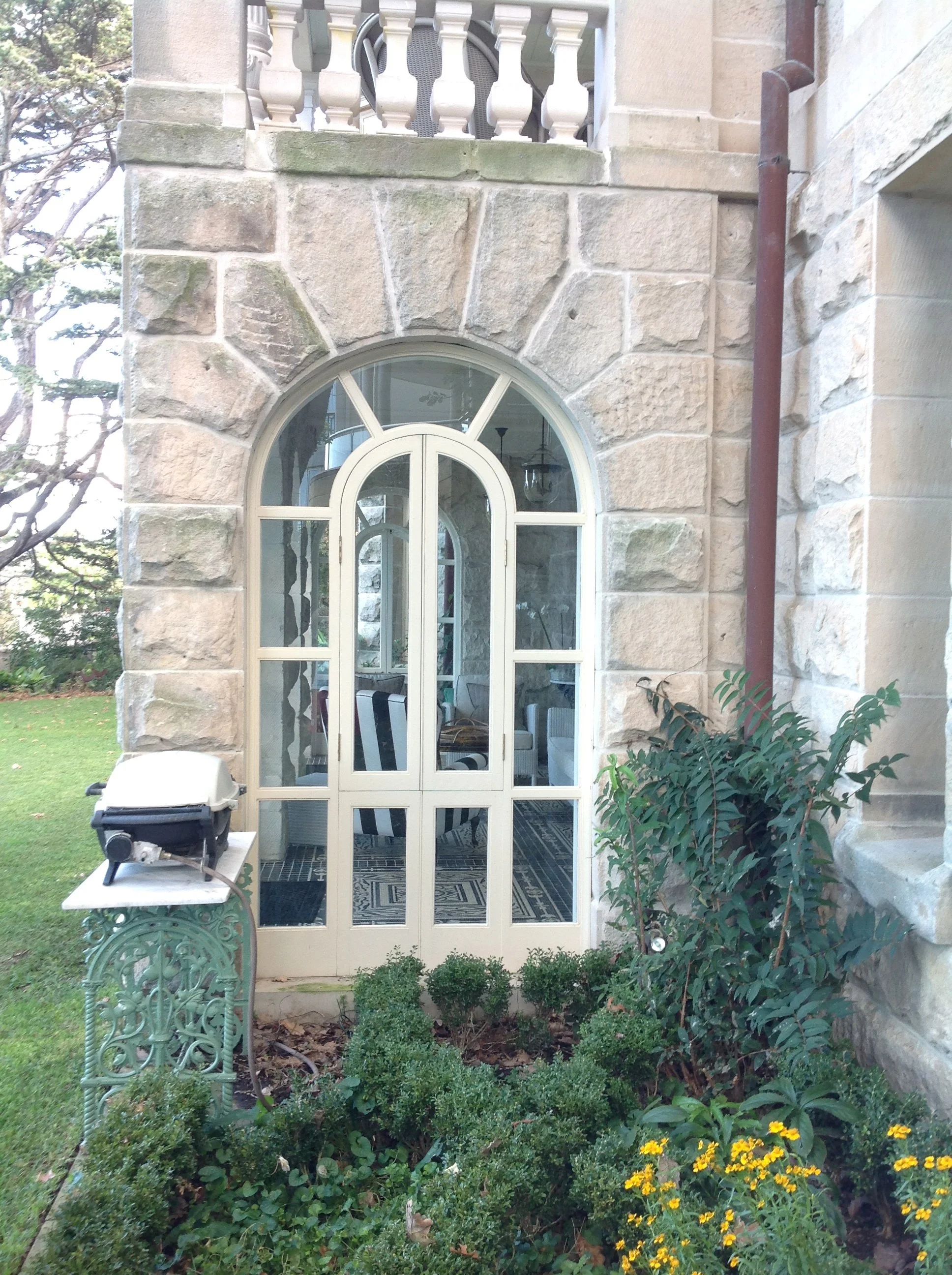 Stone building with arched window, a small barbecue on a decorative stand, plants, and flowers.