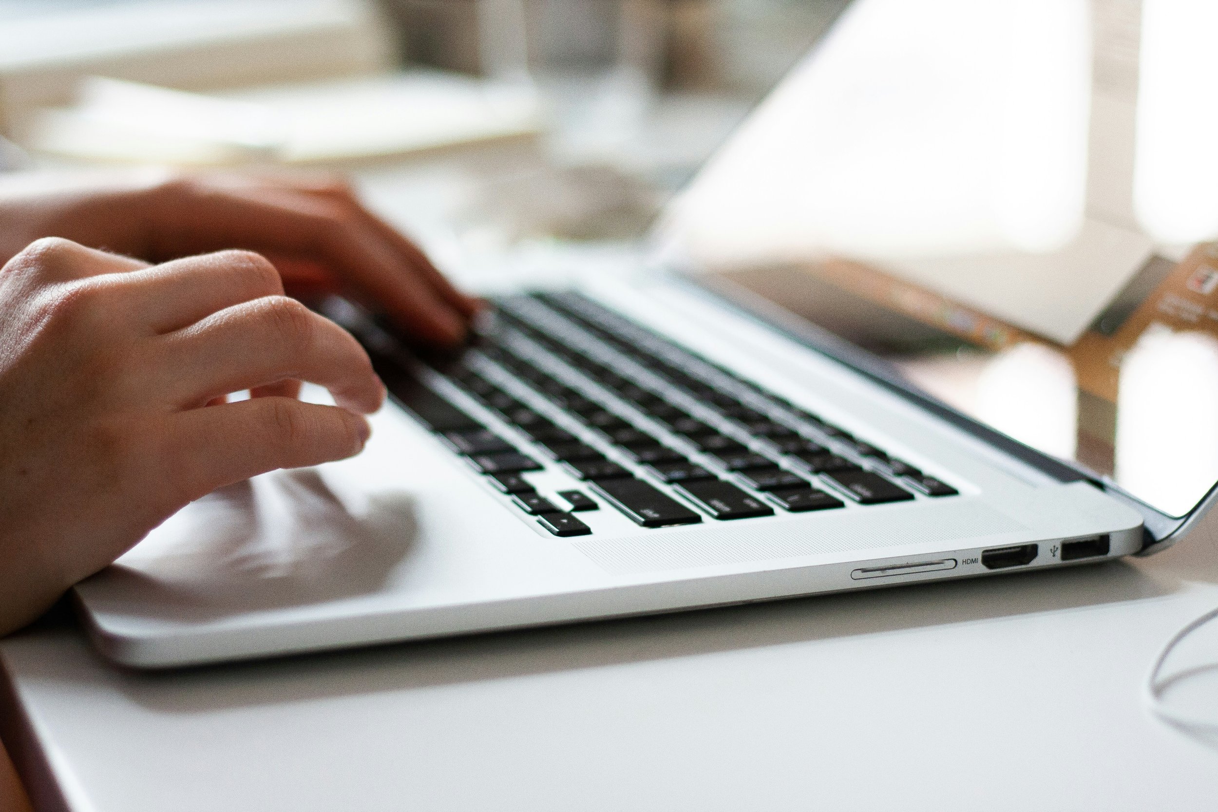 Close-up of hands typing on a laptop keyboard, with a smartphone and papers nearby on a desk.