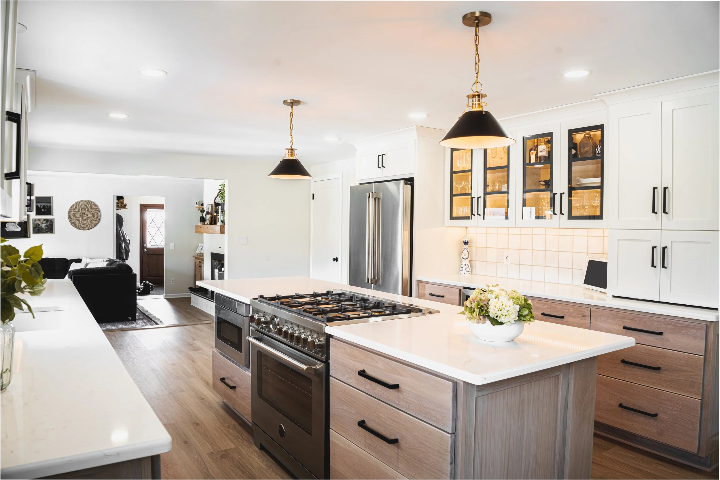 Front view of a modern two-story house with black and grey exterior, large glass doors, a landscaped garden, and a clear blue sky.