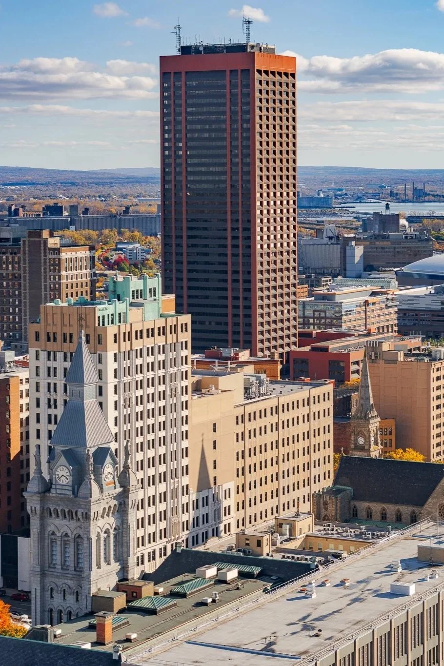 Front view of a modern two-story house with black and grey exterior, large glass doors, a landscaped garden, and a clear blue sky.