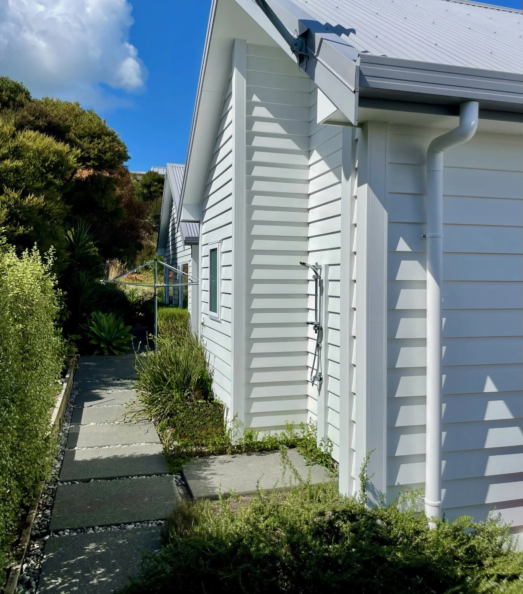 Stingray new home side elevation with white cladding and landscaping, Mangawhai