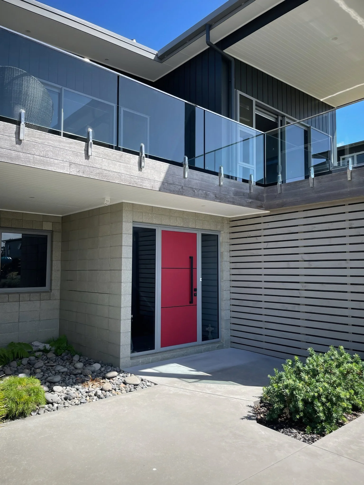 Driftwood new home build with dark cladding and bold red front door, Mangawhai