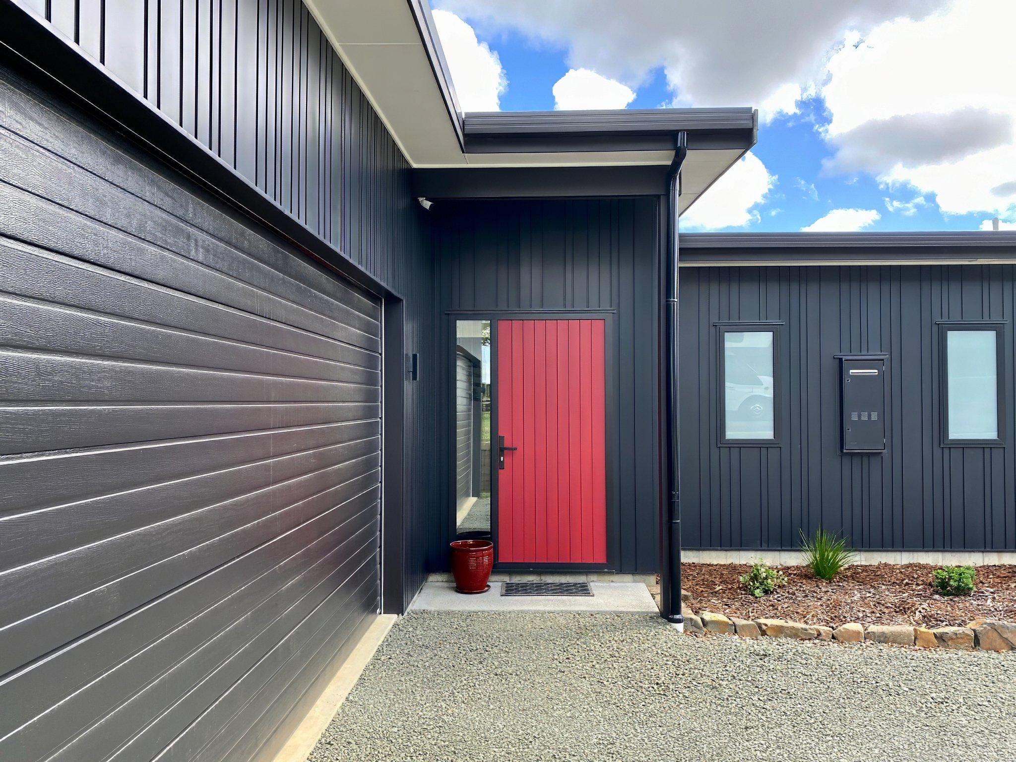 King Road luxury new home with dark cladding, garage and bold red front door, Mangawhai