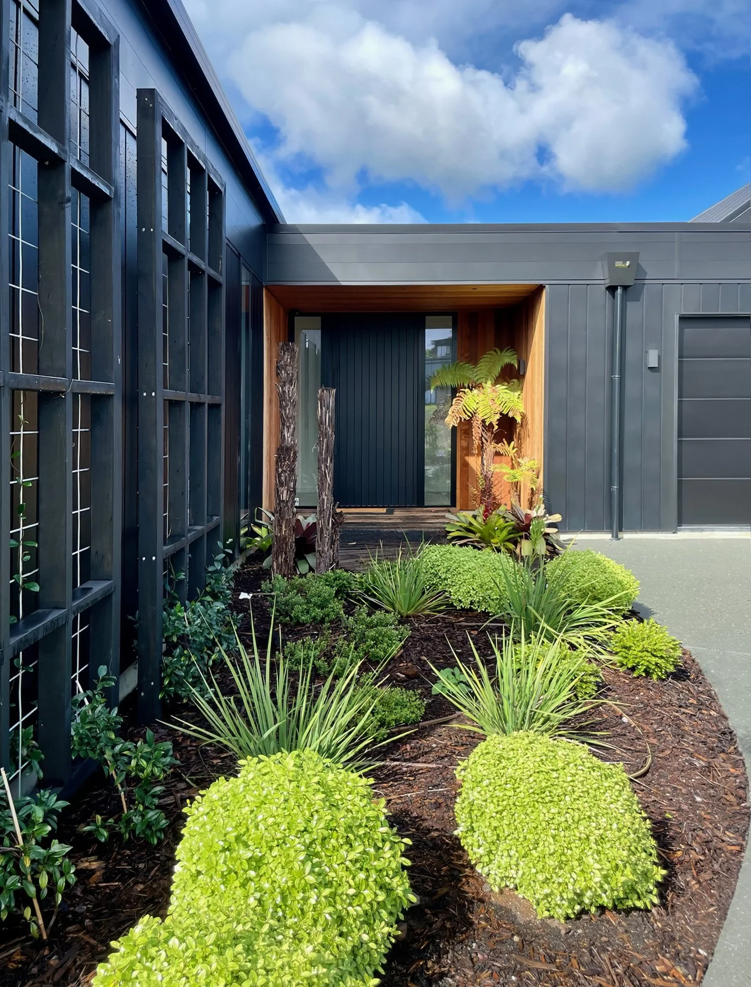 Sand Dune new home entry with tropical garden planting and dark cladding, Mangawhai