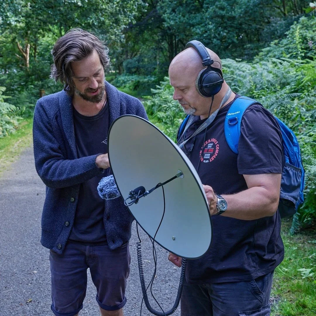 Two men examining a satellite dish outdoor in a lush green forest.