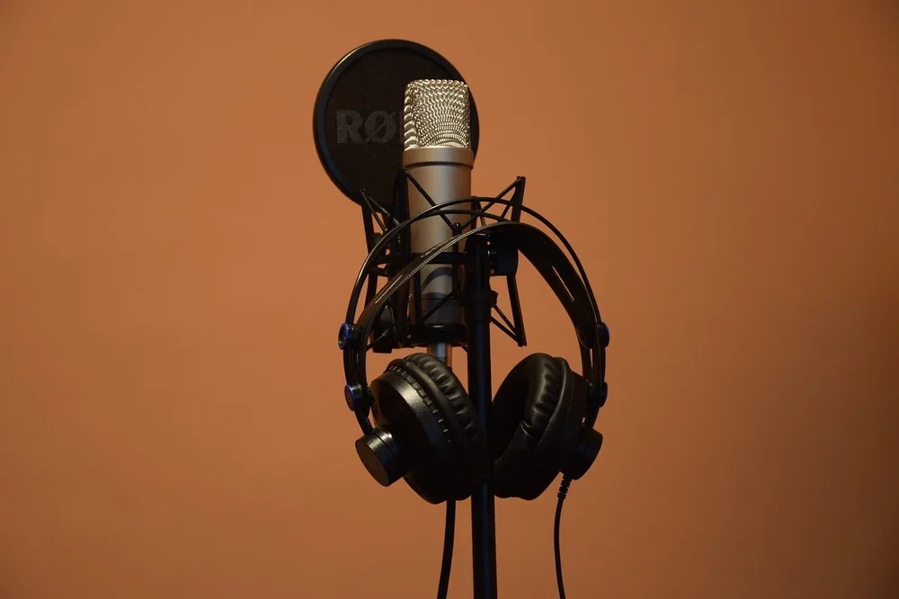 Microphone on a stand with headphones hanging, set up in a recording studio with a brown background.