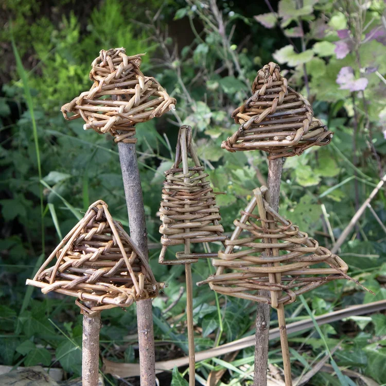 Five small woven wicker mushroom garden decorations on sticks among green plants.