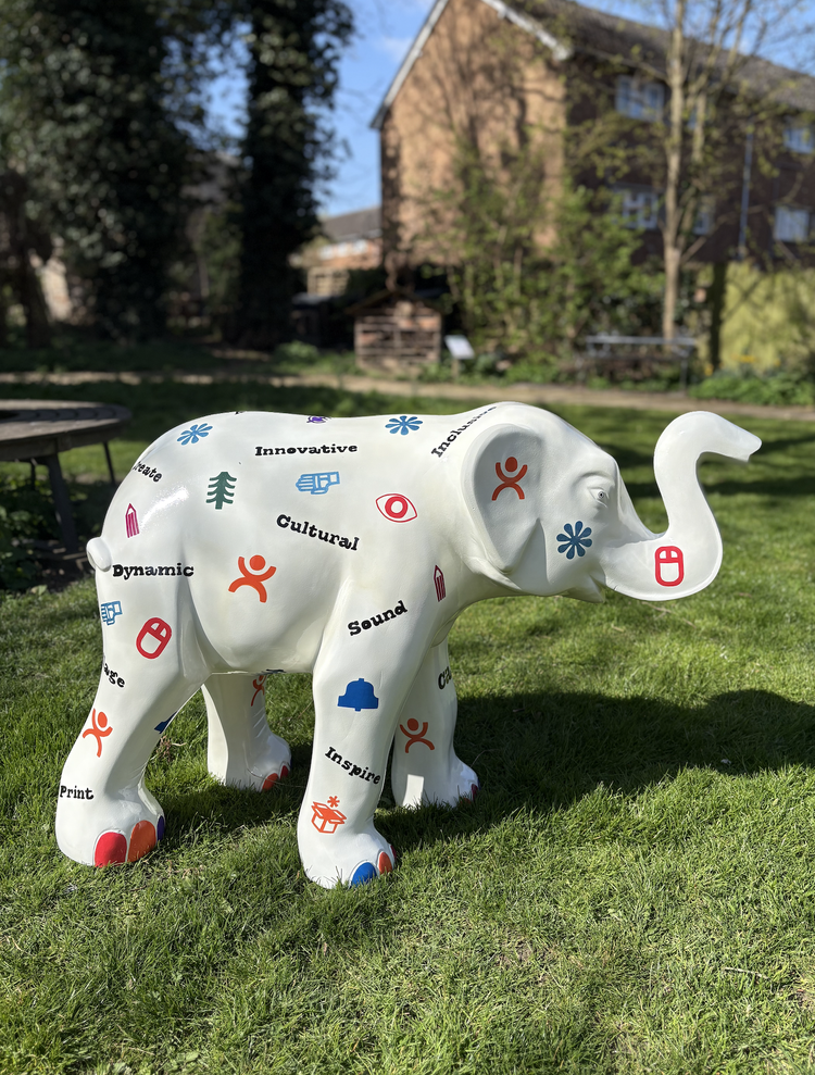 Colorful elephant-shaped sculpture outdoors on a grassy area, decorated with words and symbols like 'Innovative,' 'Cultural,' 'Sound,' and 'Inspire.'