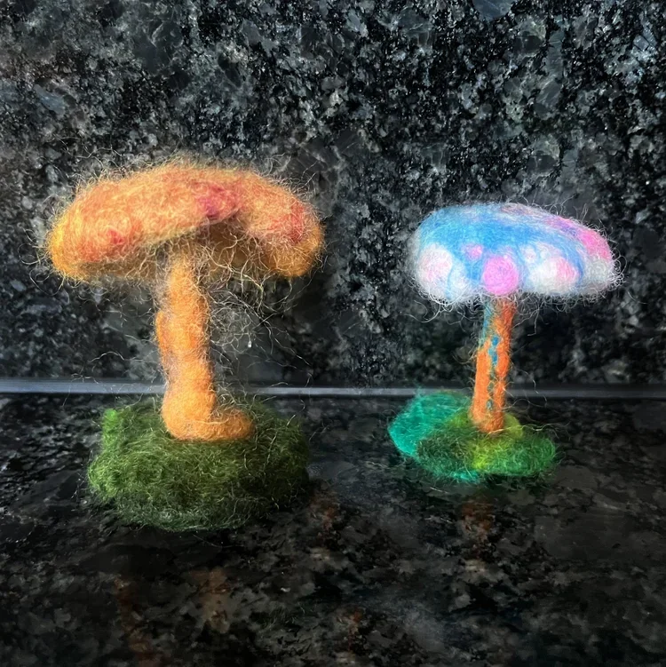 Two colorful felted mushroom sculptures on a dark, speckled granite surface.