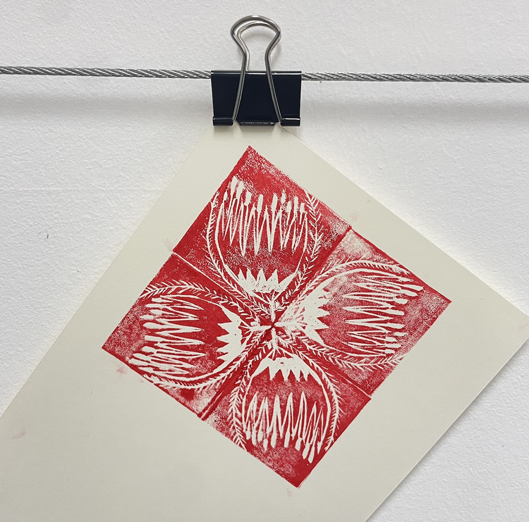 Red and white abstract art lino-print hanging with a black clip on a wire