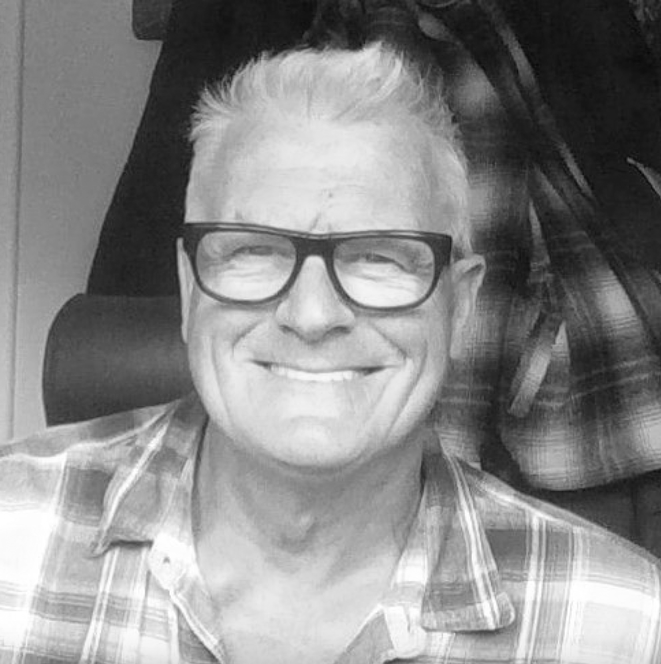 A photo of John Dimmick smiling with black glasses wearing a plaid shirt.