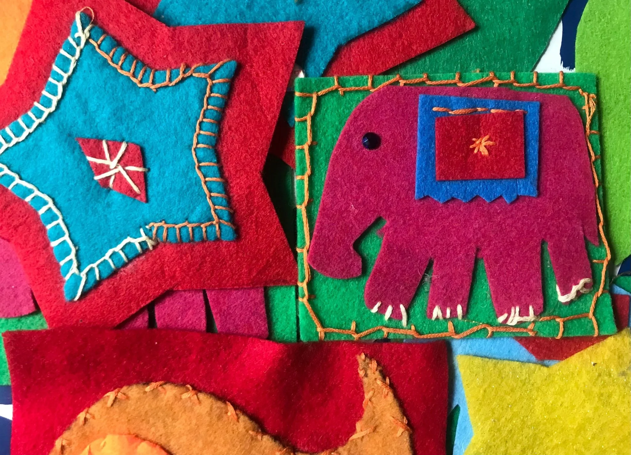 Colorful felt animal and geometric shapes, including an elephant with a square on its back, all decorated with embroidery and stitched details.