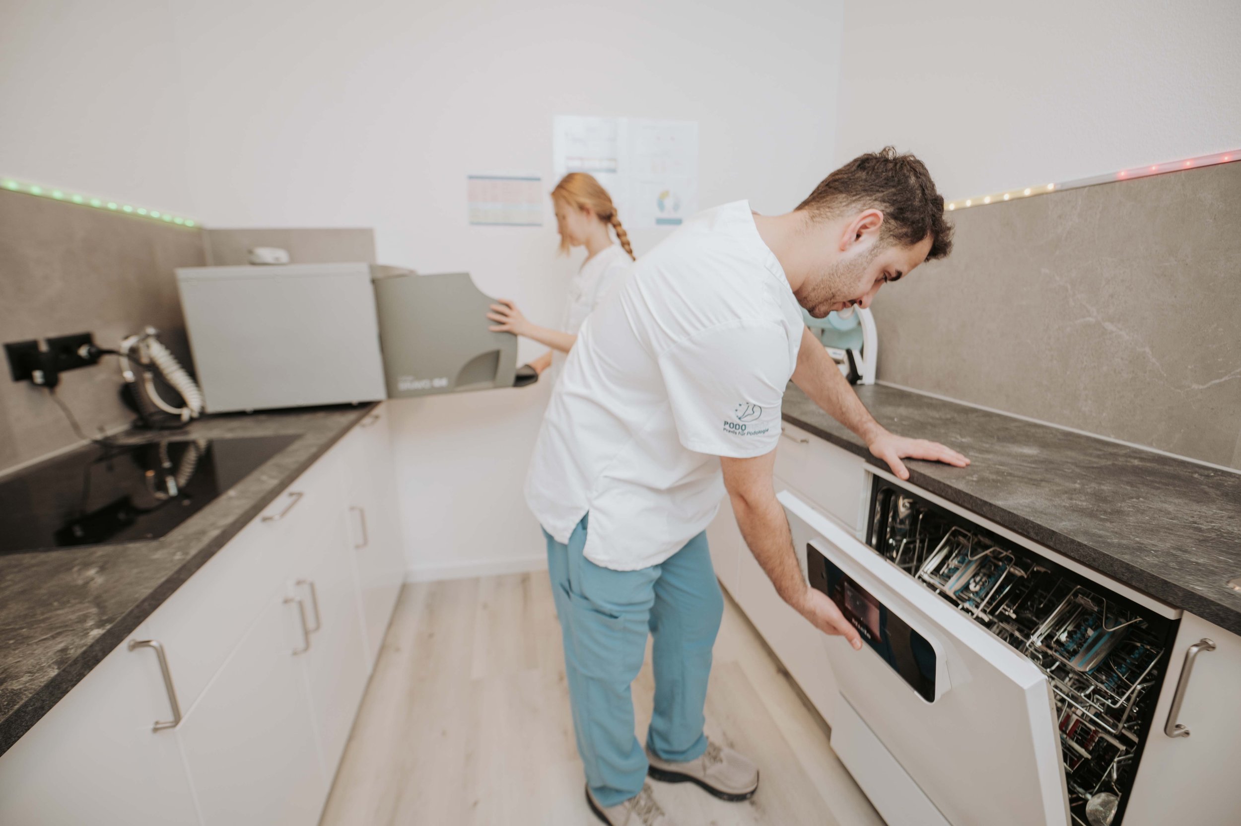Ein Mann öffnet eine Brotdose in einer modernen Küche, im Hintergrund eine Frau bei einem Computer.