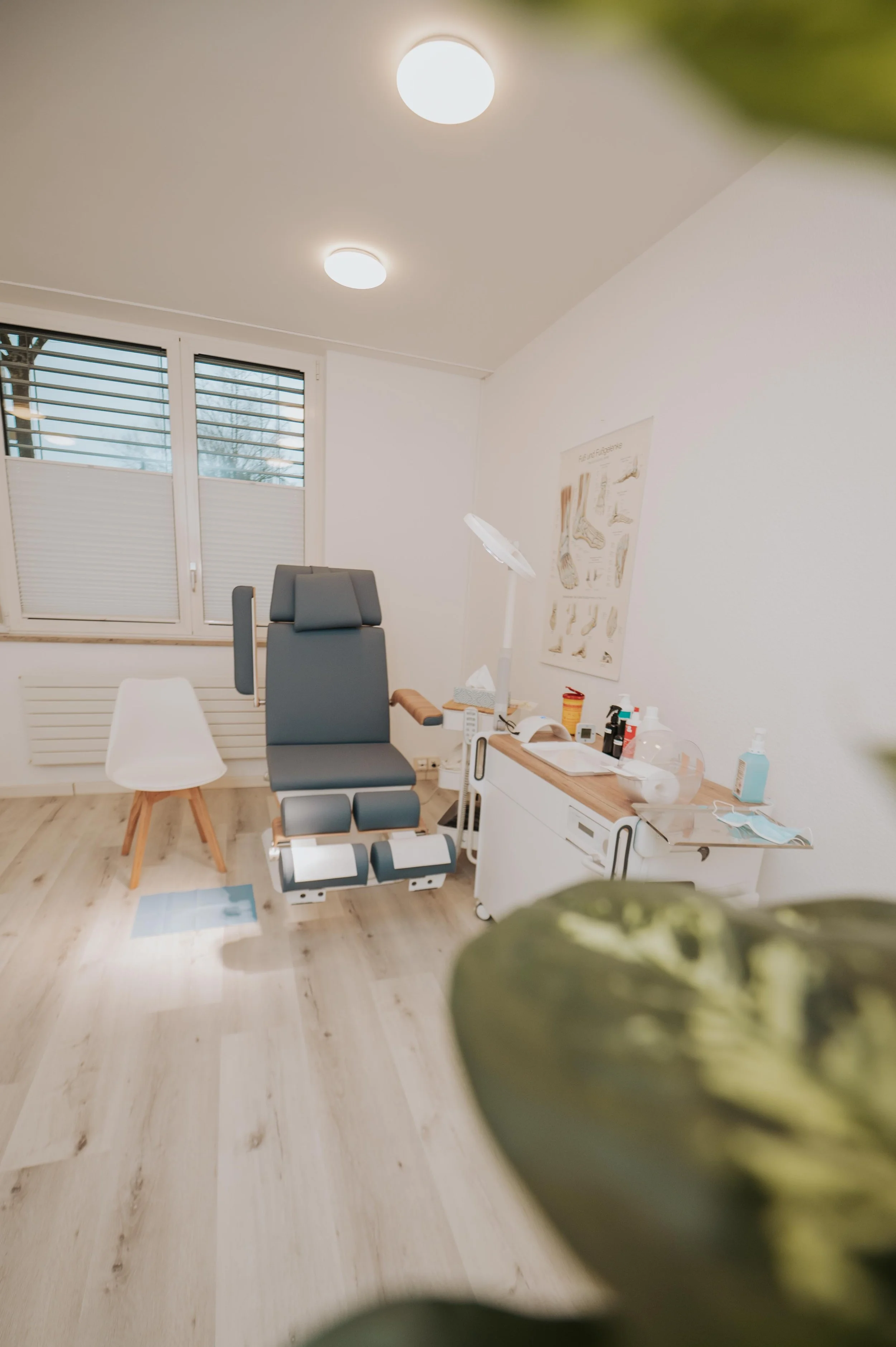 Möbel in einem Wartezimmer, darunter ein Untersuchungstisch, ein Stuhl, ein Tisch mit medizinischen Utensilien und ein Poster an der Wand.