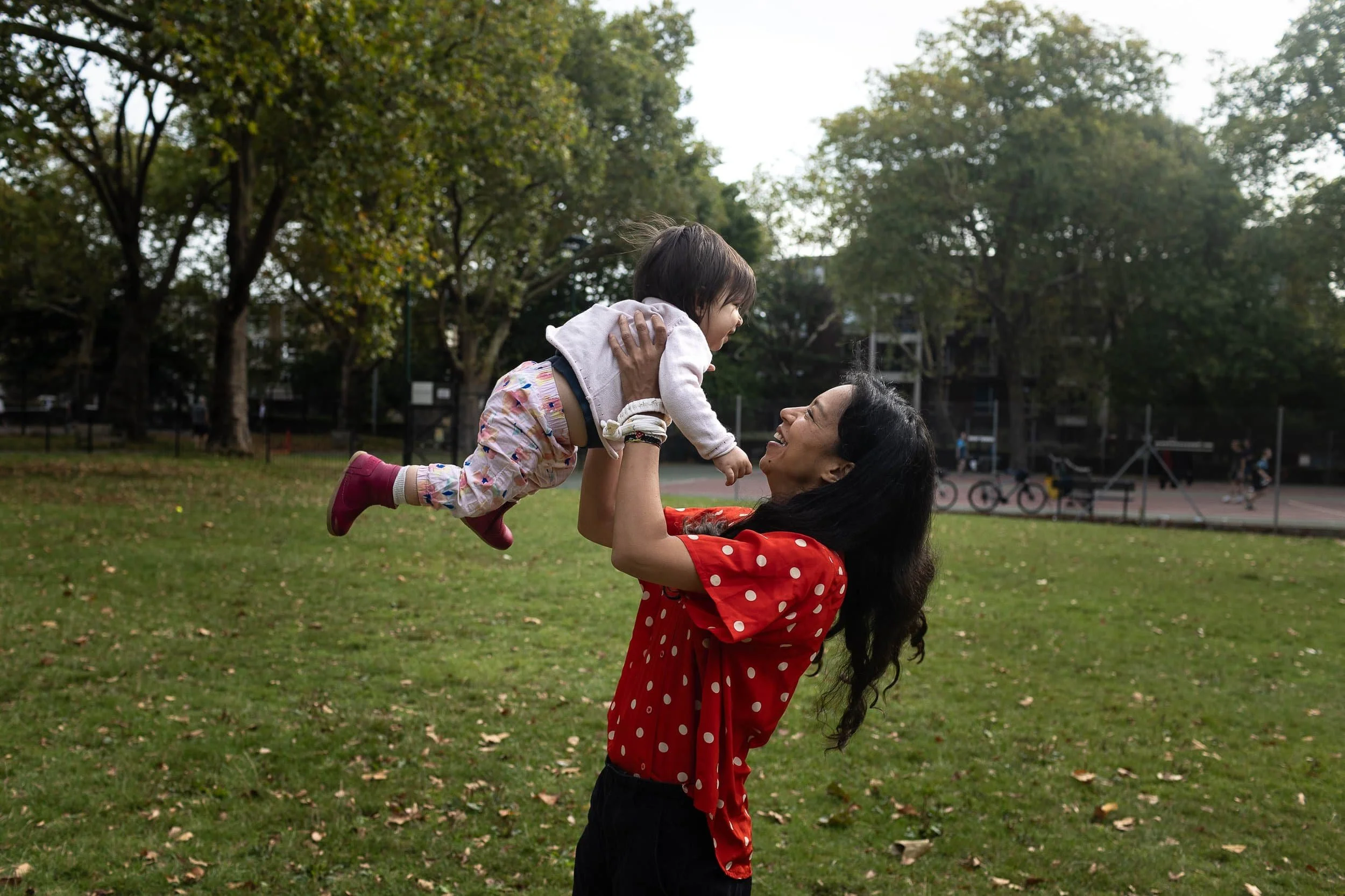A little girl being thrown in the air by her mum in Highbury Fields park