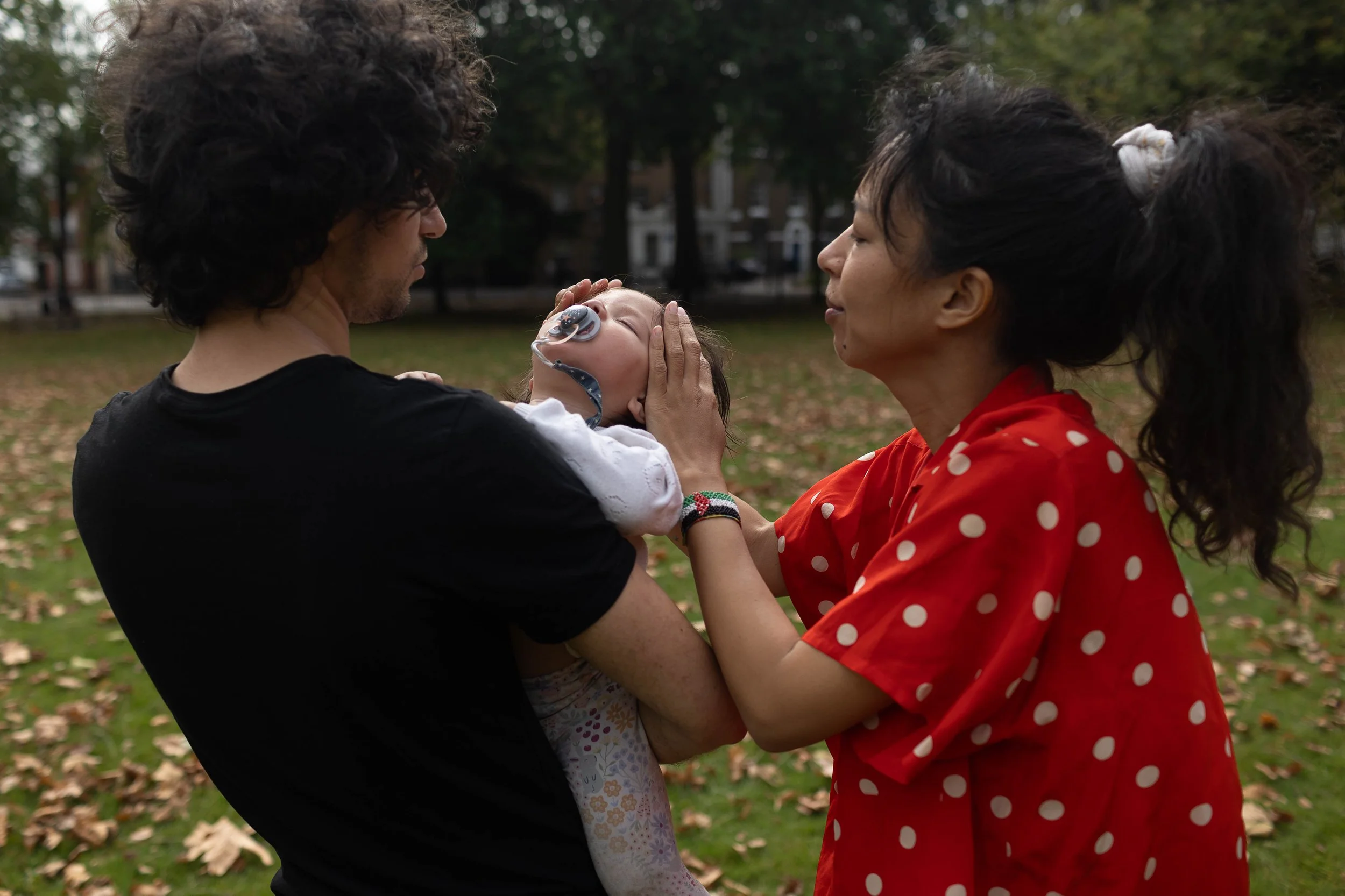 A sleeping toddler being held by her mum and dad in the park