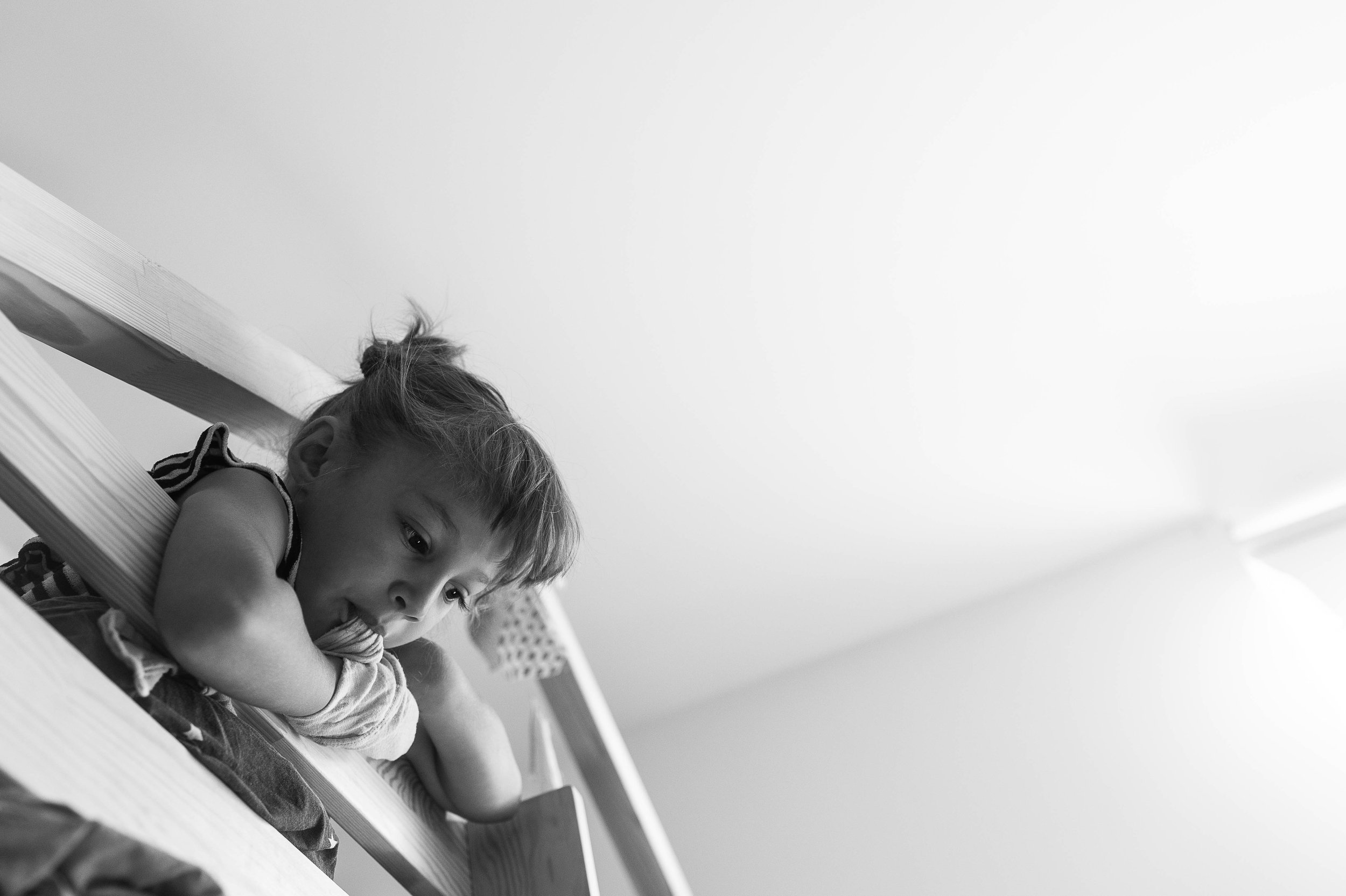 Regenerate alt text copyIconcrossIconBlue A young girl rests her chin on her arms, leaning over a wooden railing, looking pensive in a bright, minimal room.