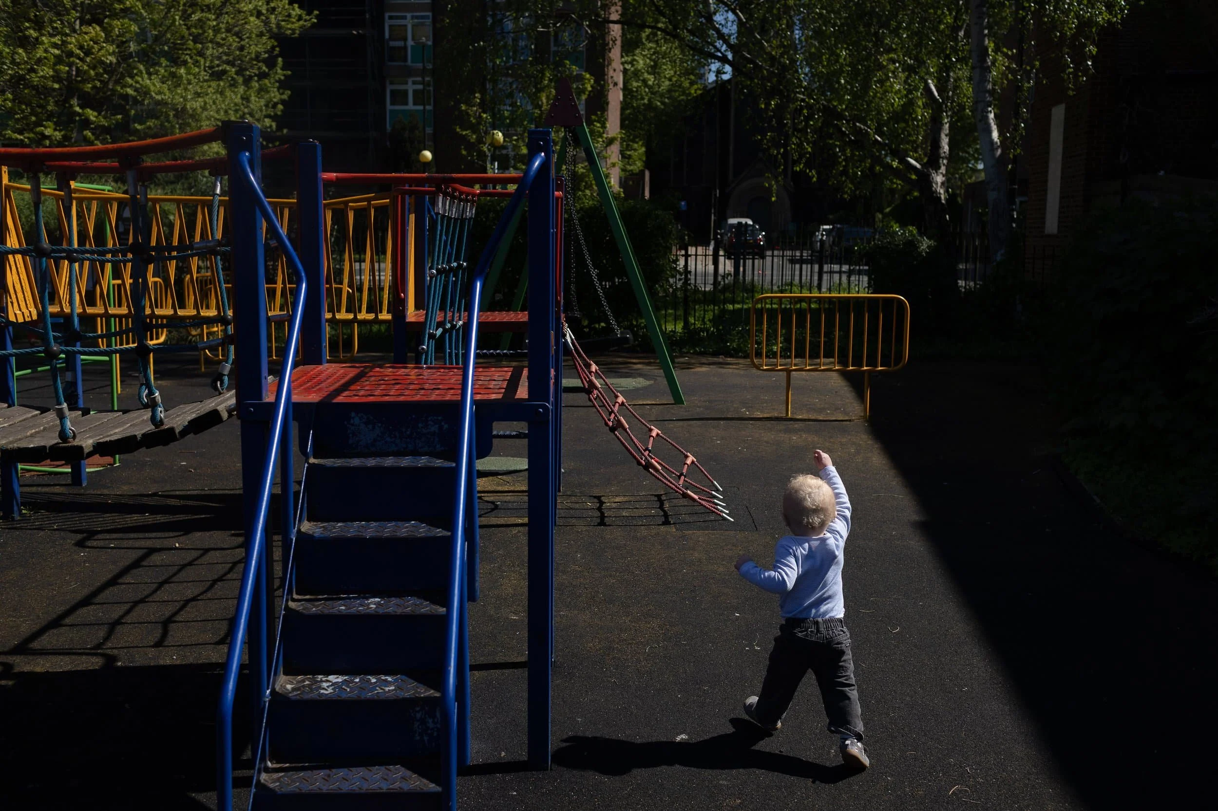 A small child walks towards a colourful playground climbing frame reaching up with one arm