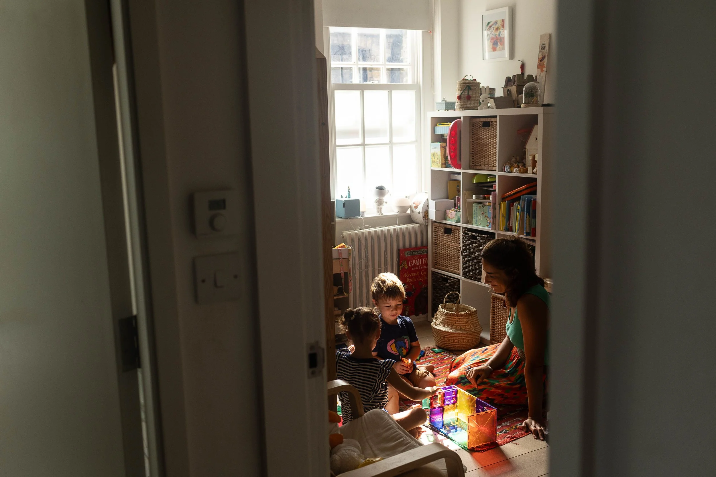 A Tufnell Park family photographer captures a woman and two children playing with colorful blocks in a cozy, sunlit North London room.