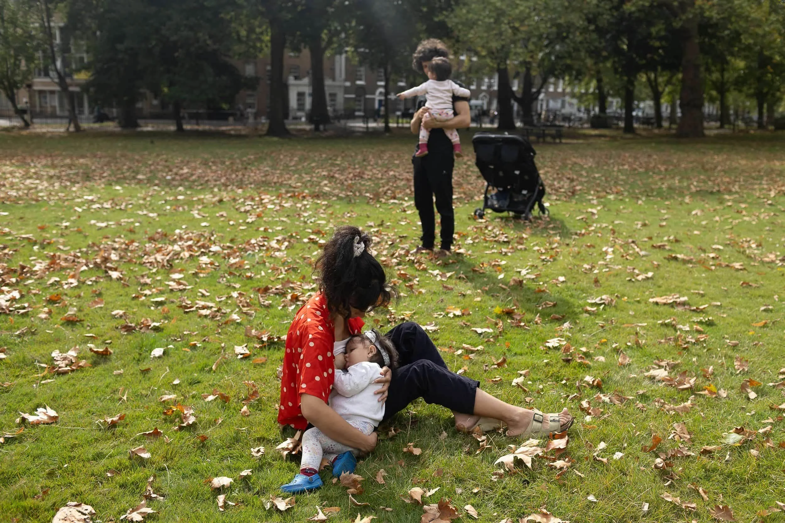 Breastfeeding twins in Highbury fields park during a family photo shoot