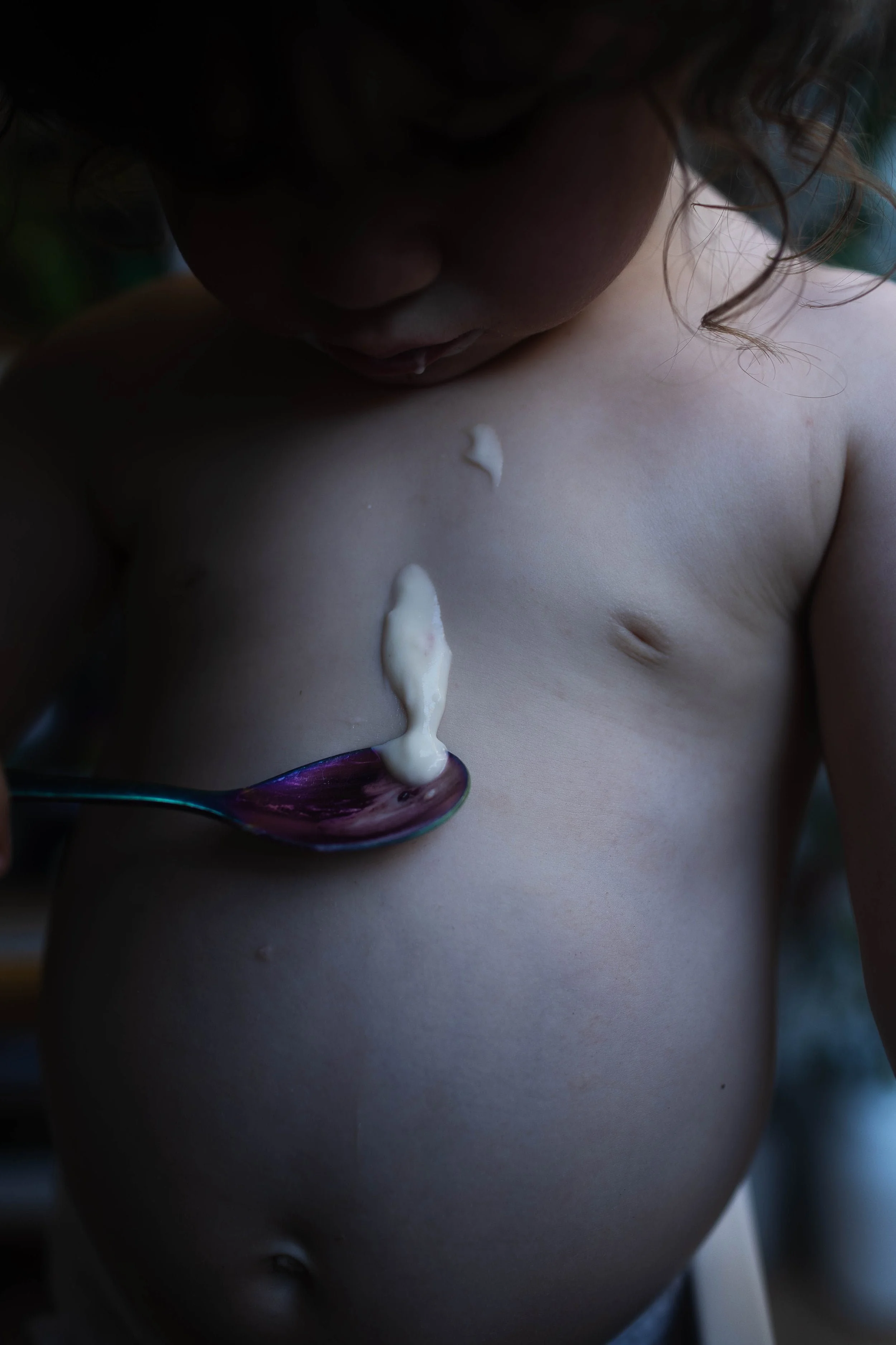 A baby girl drops yoghurt on her bare tummy during family photo session