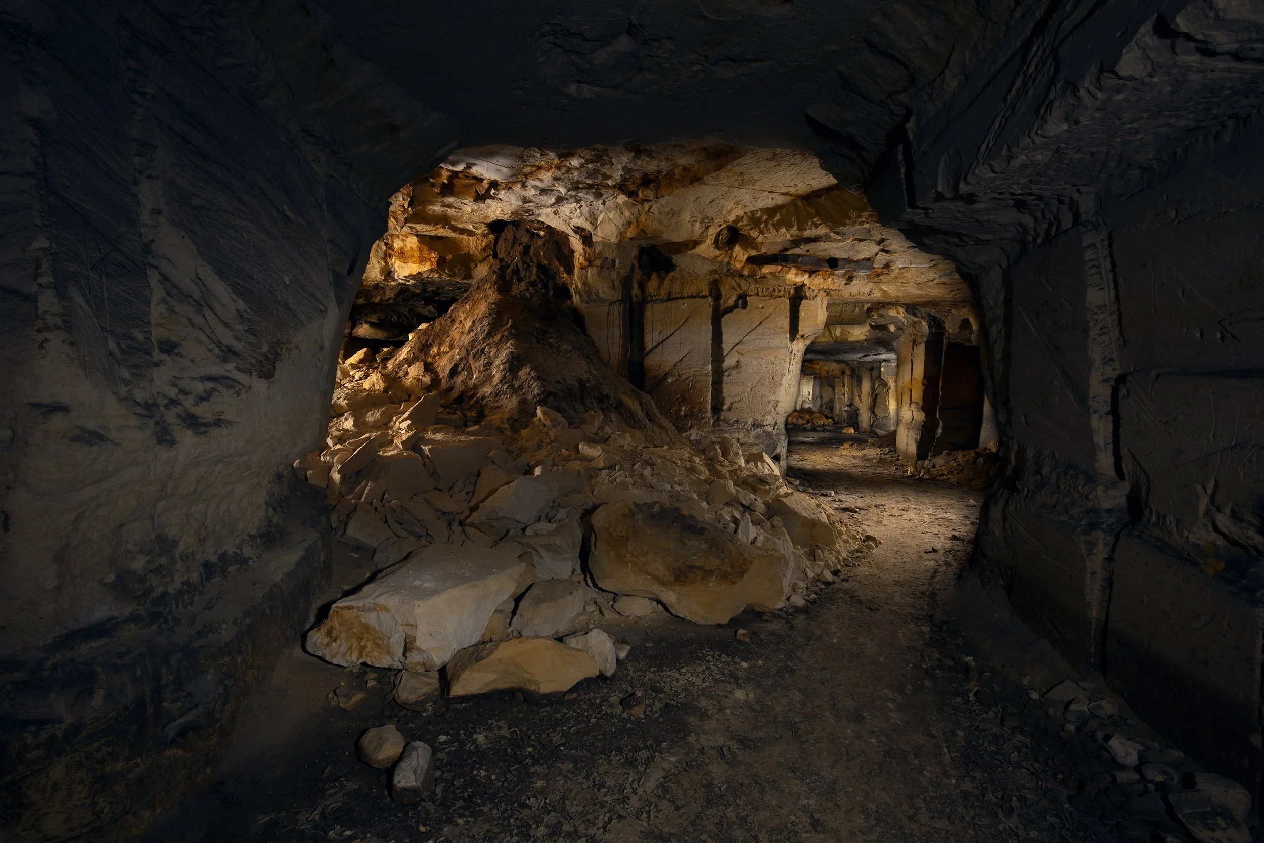 Ondergrondse mijnschacht met rotswanden en een modderige vloer, verlicht door een zacht oranje licht.