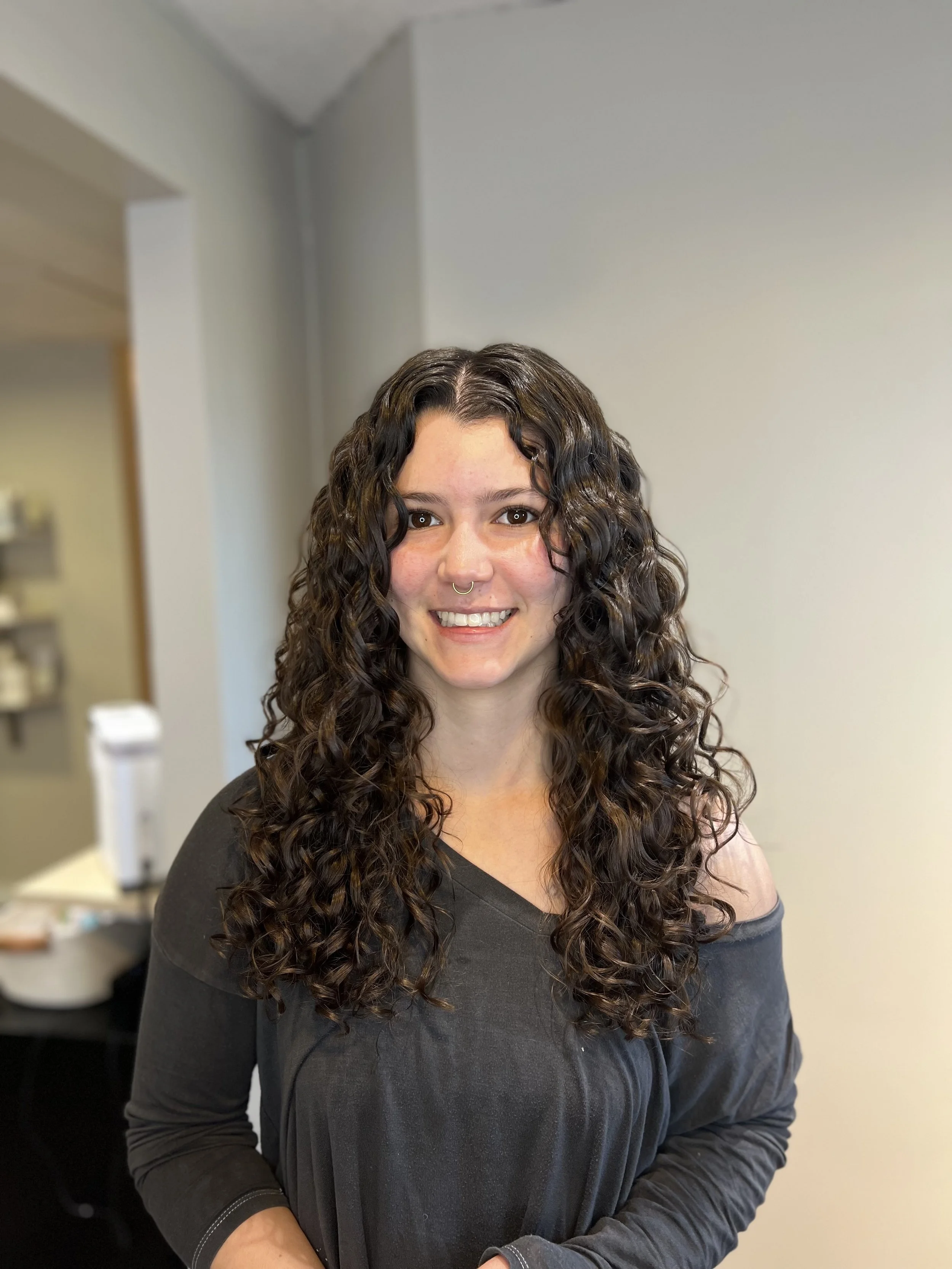 A happy client with shiny, defined curls after receiving hair treatments and a haircut.