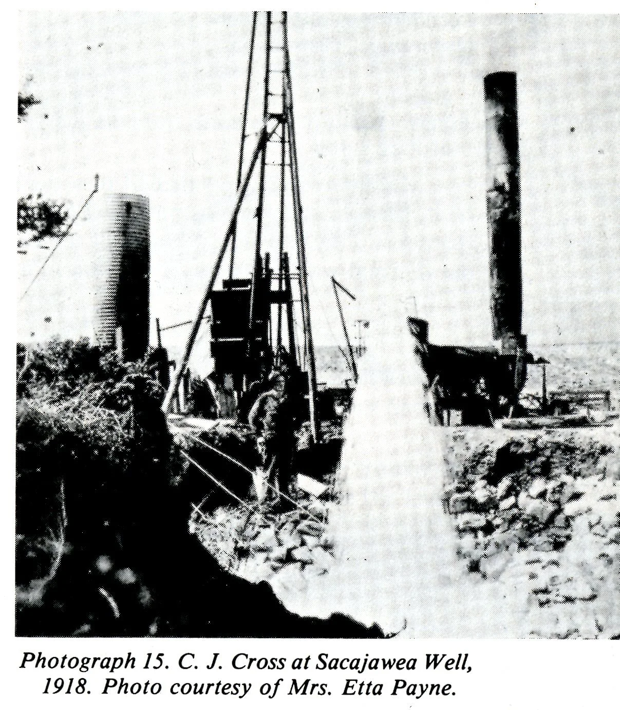 Historical black and white photograph of a well with wooden structures and equipment in 1918, part of a scene at Saca ja wea Well, with smoke and chimneys in the background.