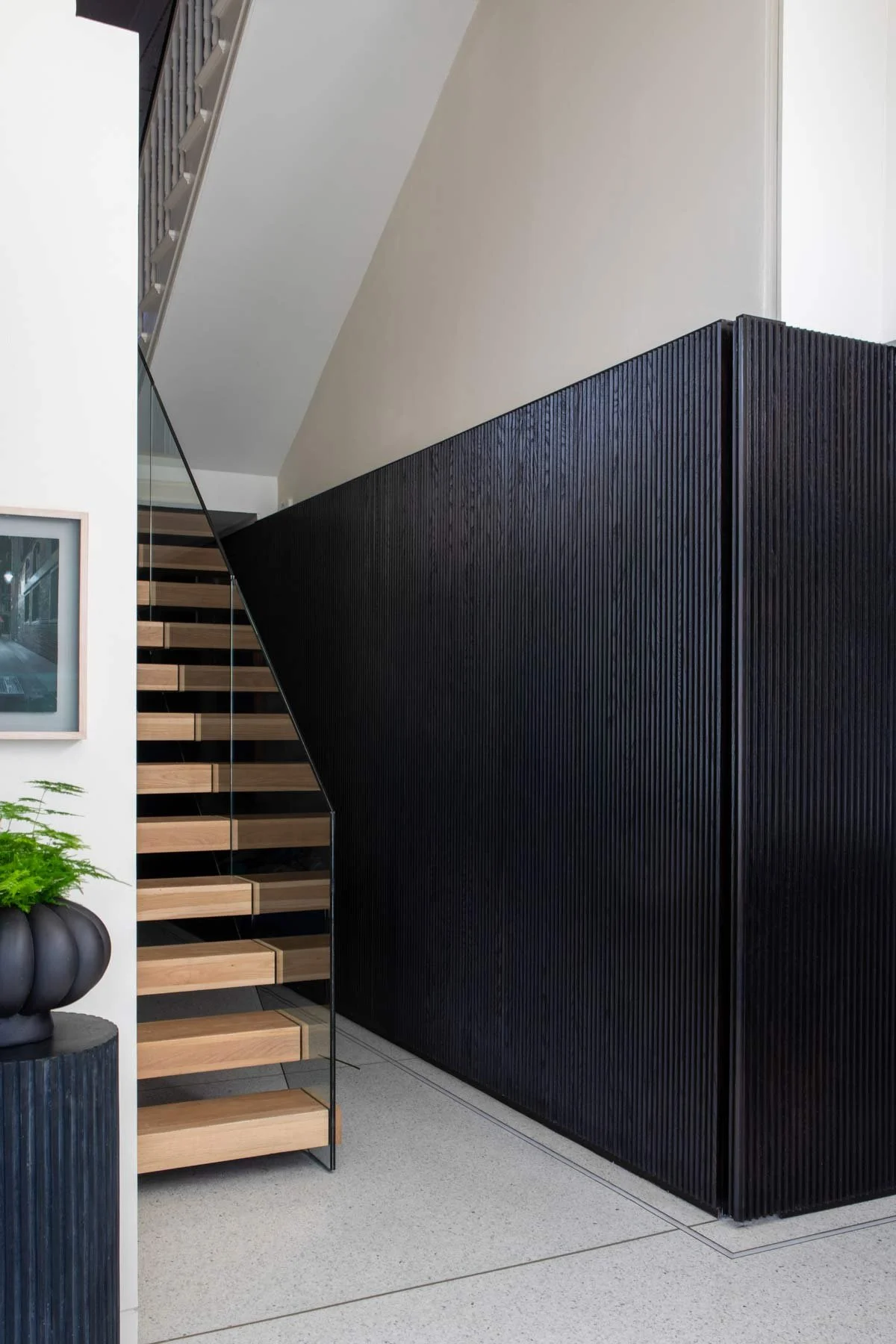 detail of wood panelled wall beside a glass and wood staircase