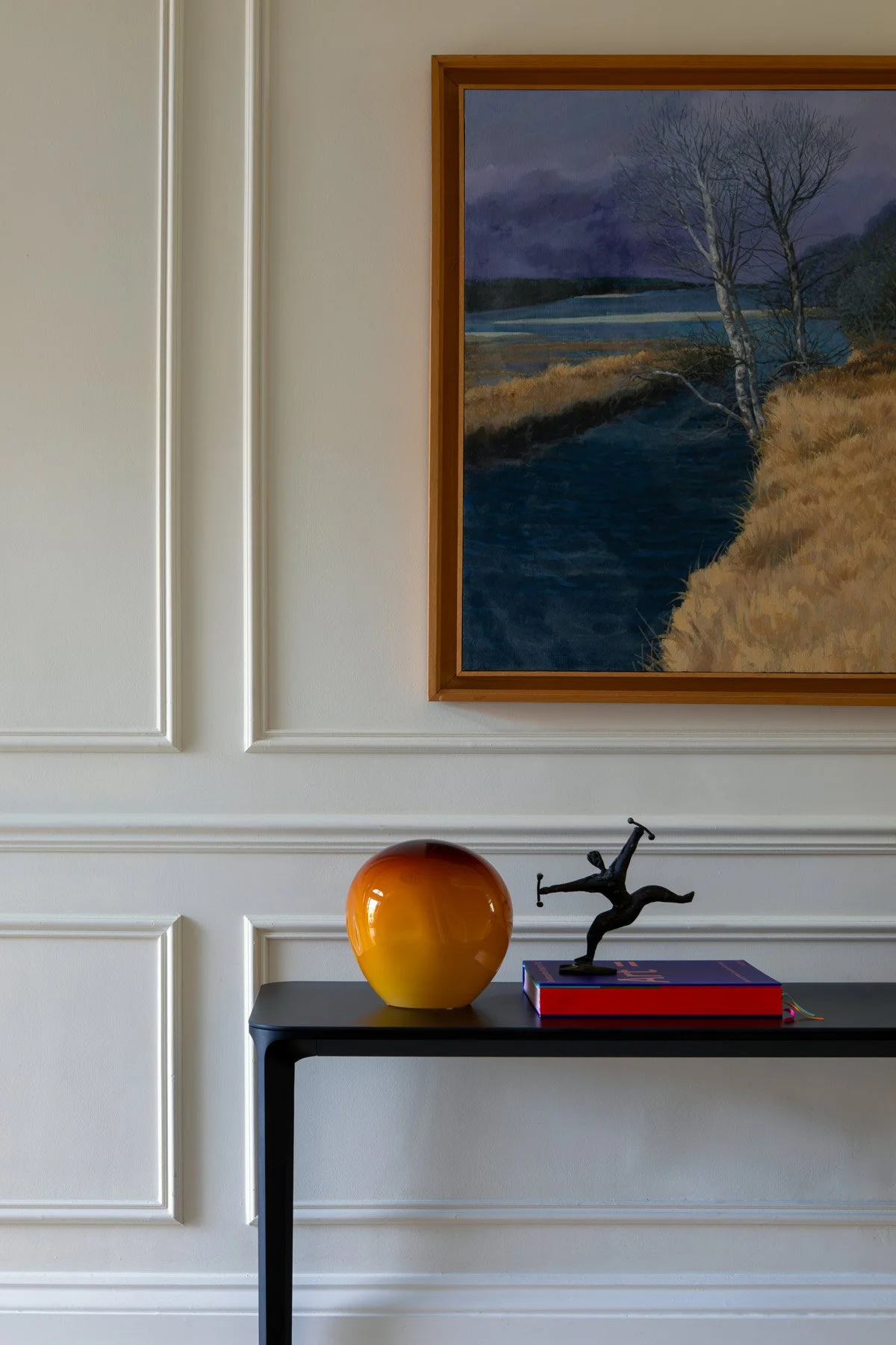 Close up of side table, with orange round vase, a book and a statue on top