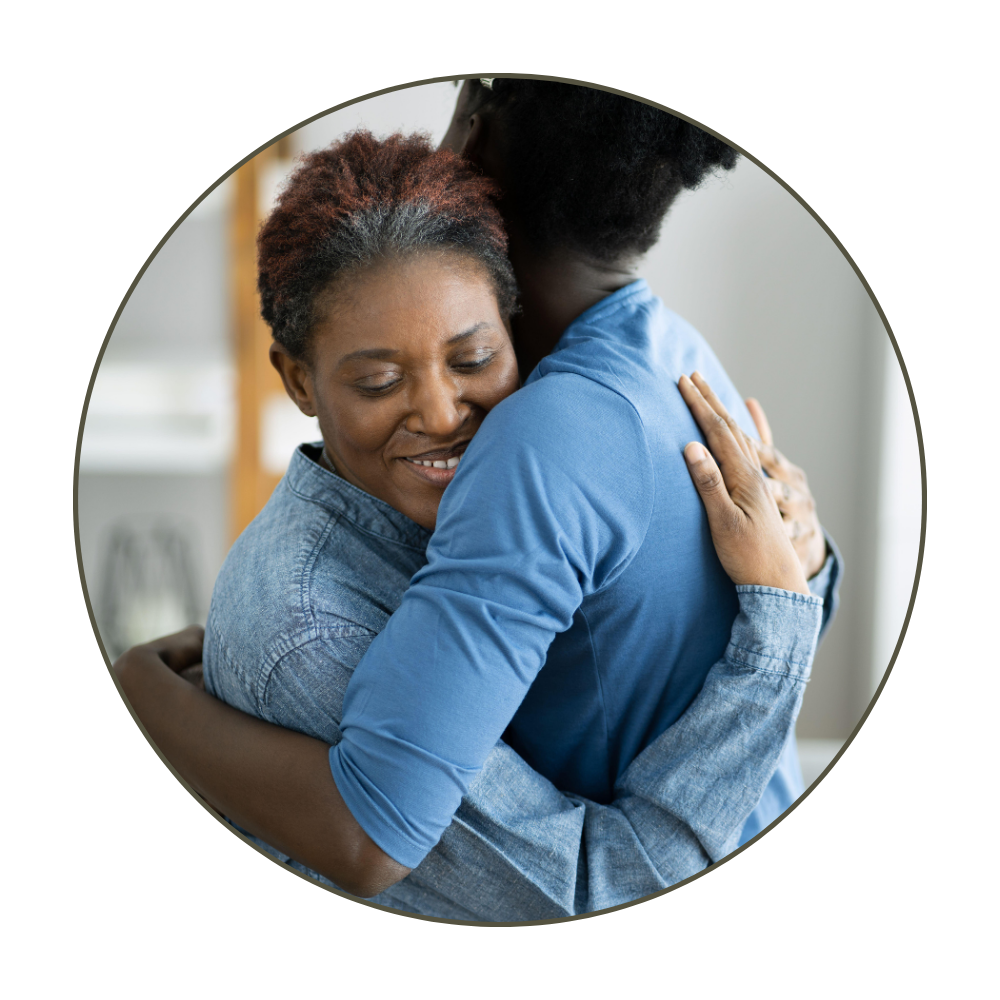 Two women hugging warmly, smiling, in a cozy room.