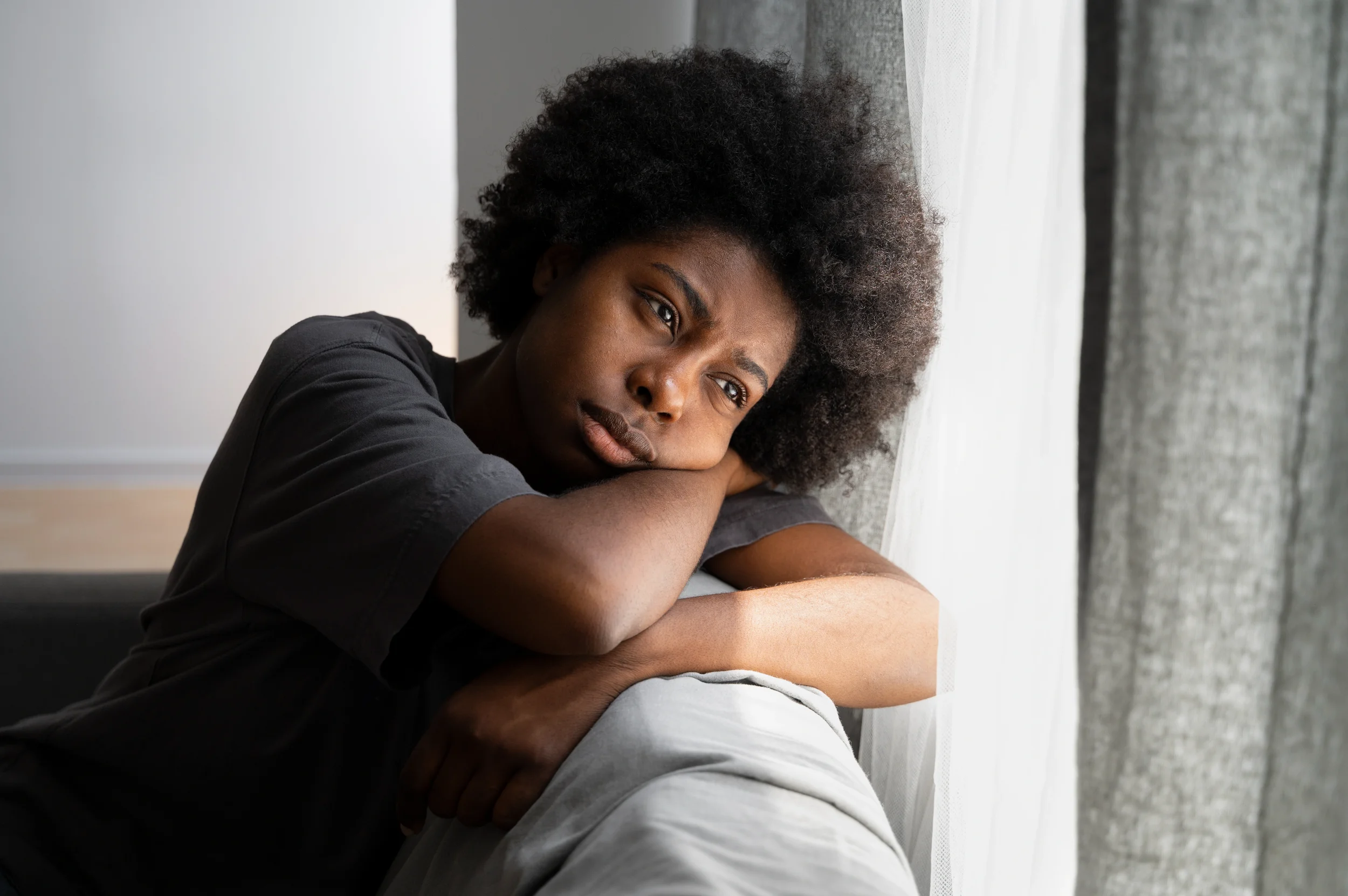 Black woman resting her head on her arms looking emotionally drained, representing persistent sadness and emotional numbness during grief