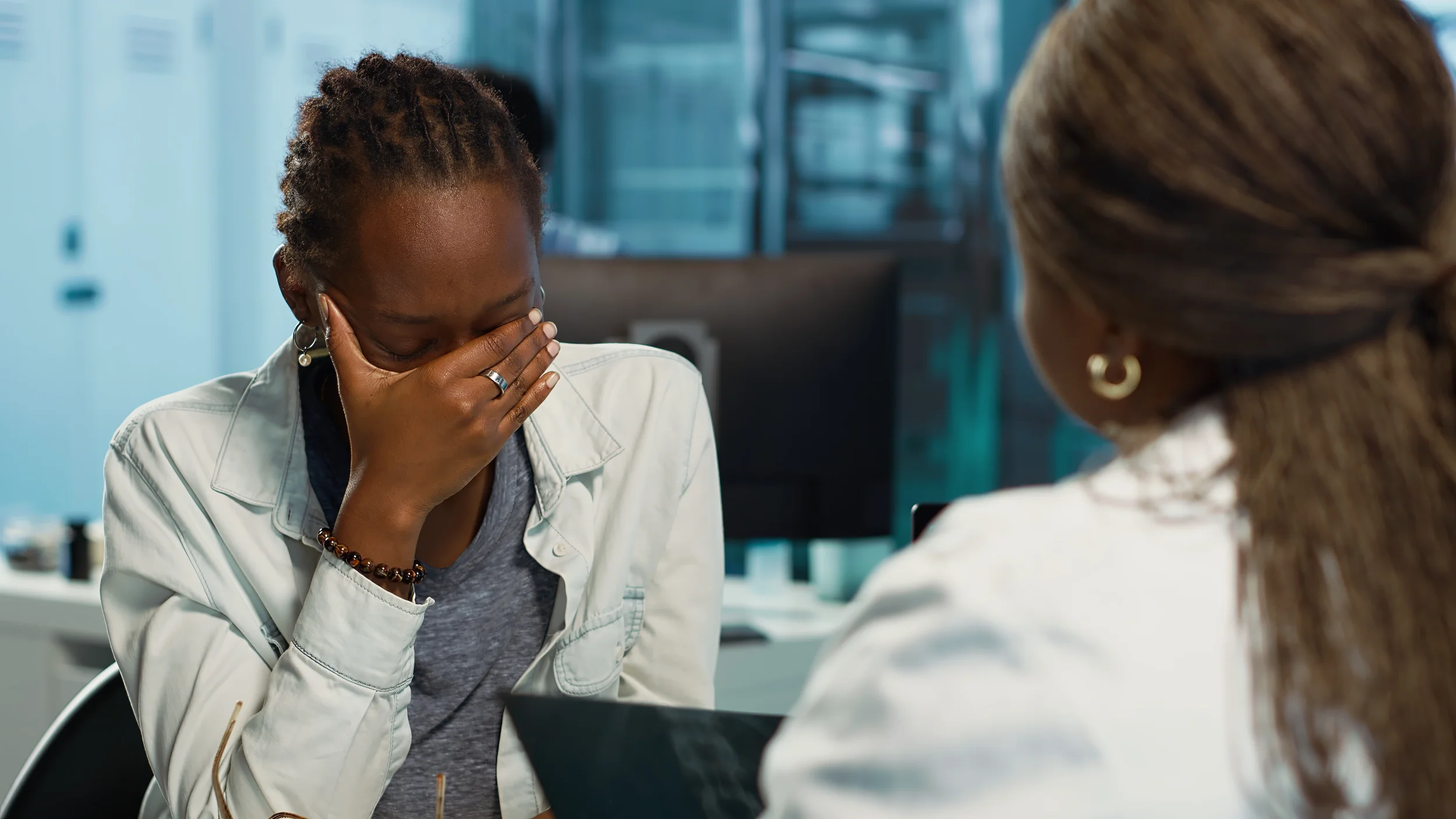 Black woman sitting alone covering her face in distress, representing emotional withdrawal and isolation while grieving