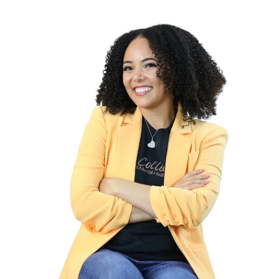 A woman with curly black hair wearing a yellow blazer, black shirt, and blue jeans, smiling with arms crossed against a black background.