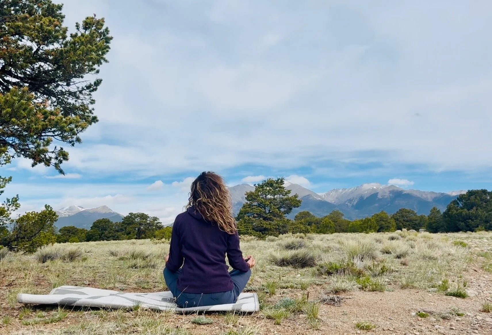 woman sitting with her back to the camera looking out at a mountain landscape, reflecting on burnout during a solo road trip
