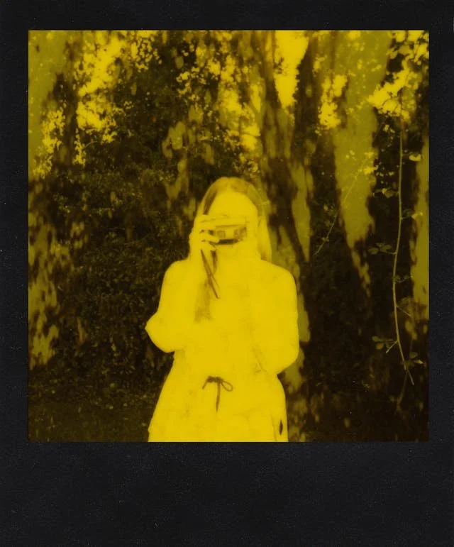 Polaroid of a woman in a light dress holding a camera in front of her face, surrounded by trees. Part of an ED recovery quote series.