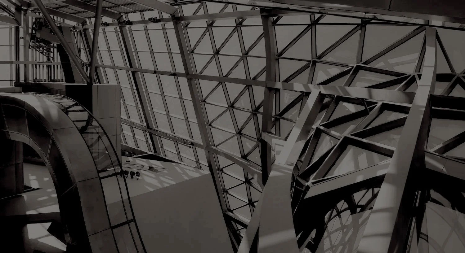Interior view of a modern building with an intricate steel and glass architectural design, including spiraling ramps and geometric patterns.