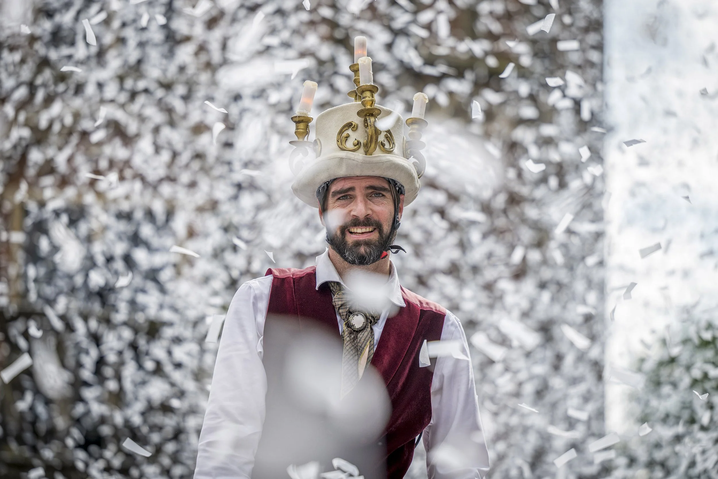 Man in costume met kroon en kaarsen op hoofd tijdens feestelijke viering, vallende confetti, bos met witte sneeuw op de achtergrond.