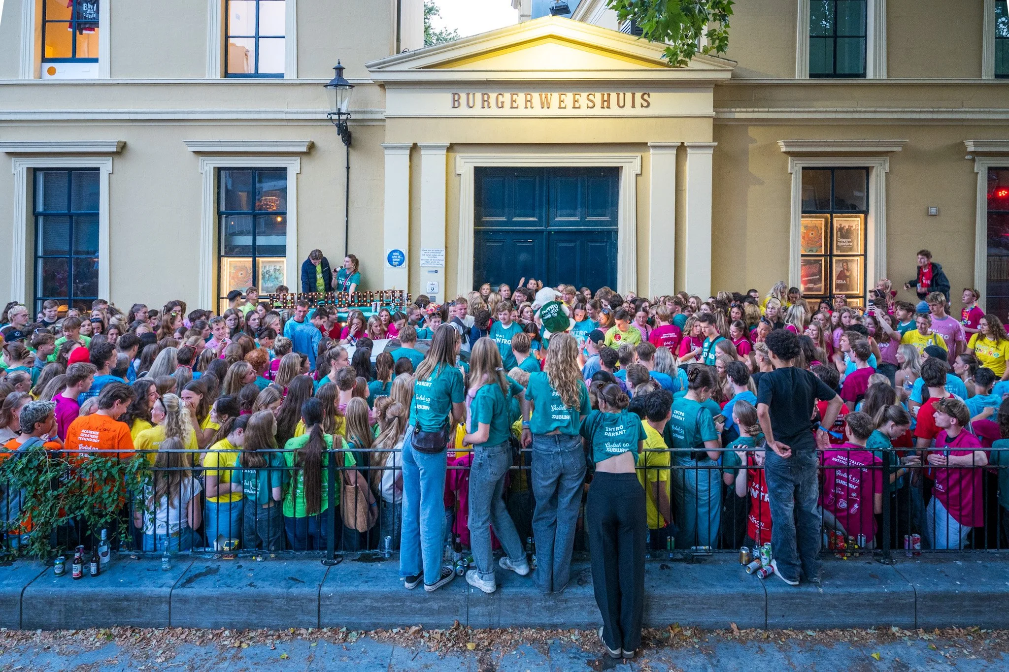 Een grote groep jongeren verzameld voor het Burgerweeshuis, mogelijk voor een evenement of viering.