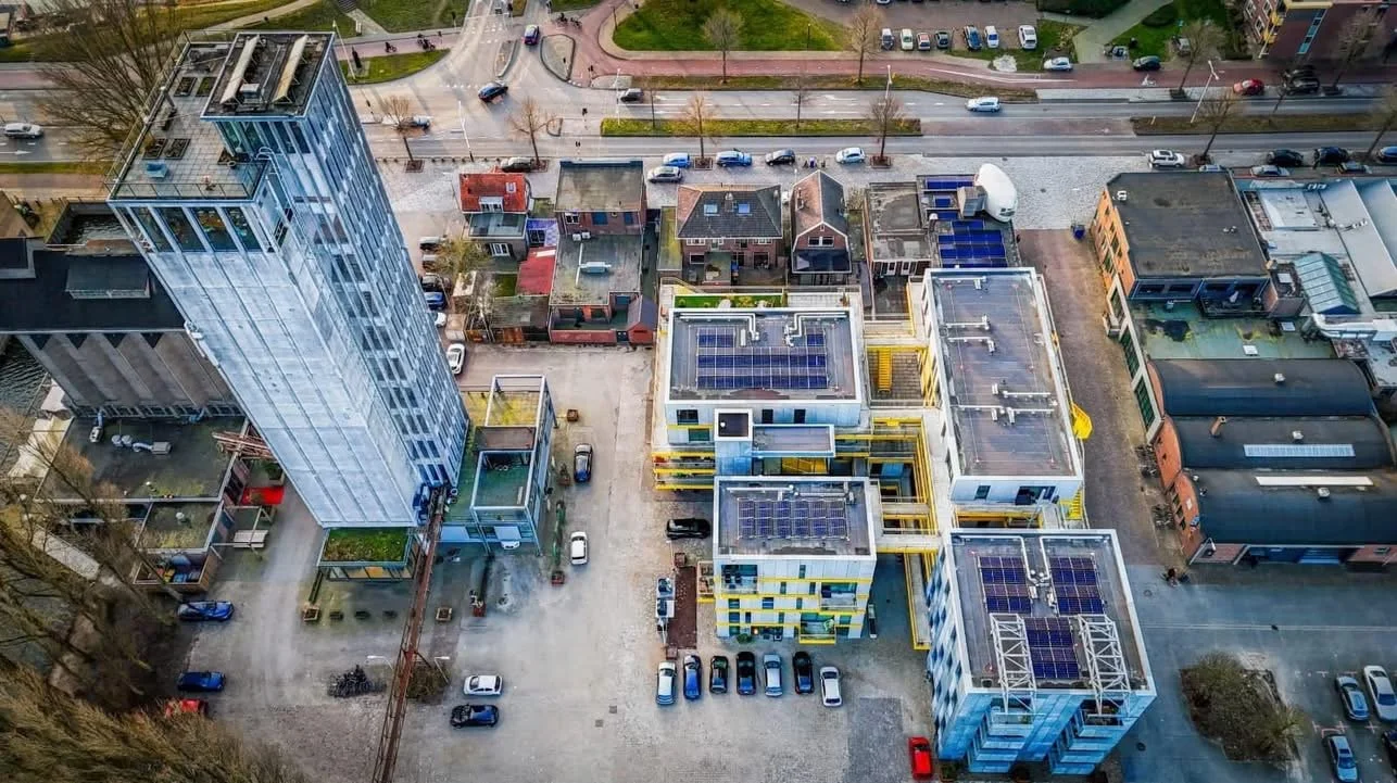 Luchtfoto van een stedelijk gebied met moderne gebouwen met zonnepanelen, parkeerplaatsen en een groenvoorziening.
