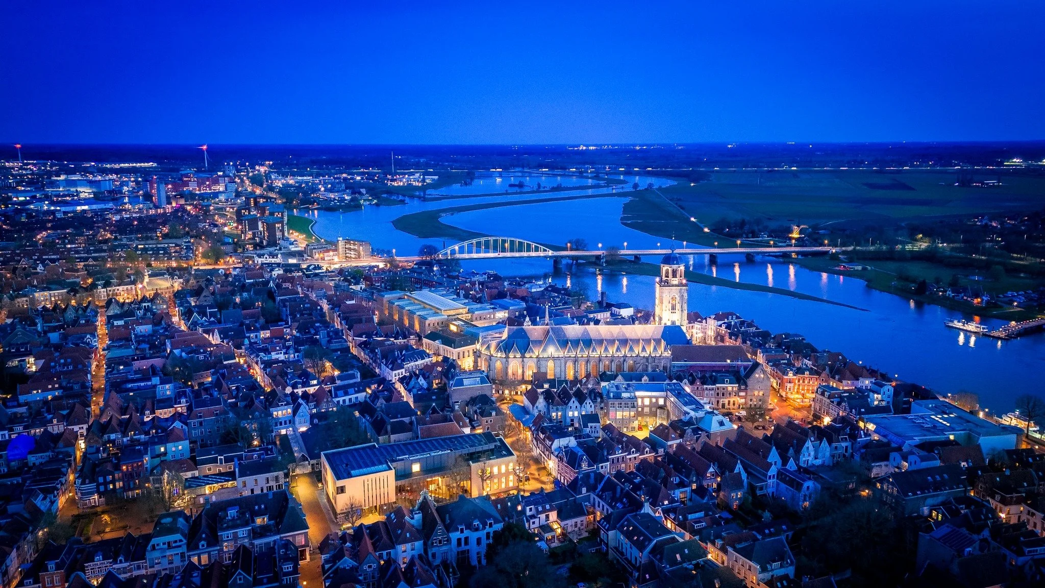 Luchtfoto van een stad bij nacht met een rivier en meerdere bruggen, omringd door inventieve verlichting en gebouwen.