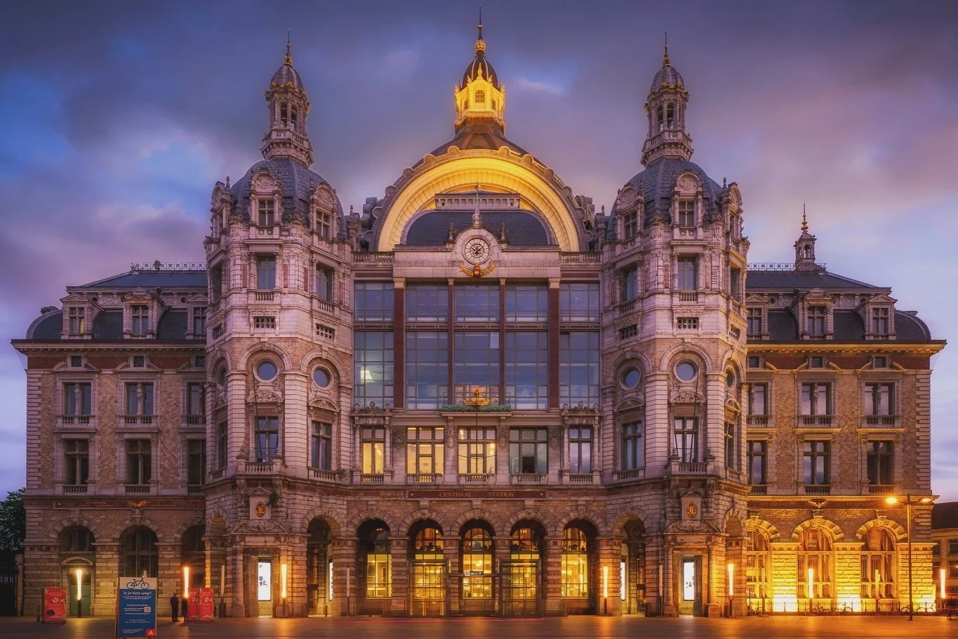Een historisch gebouw met een neoclassicistische architectuur, verlicht in de avond, met meerdere torens en een grote centrale koepel.